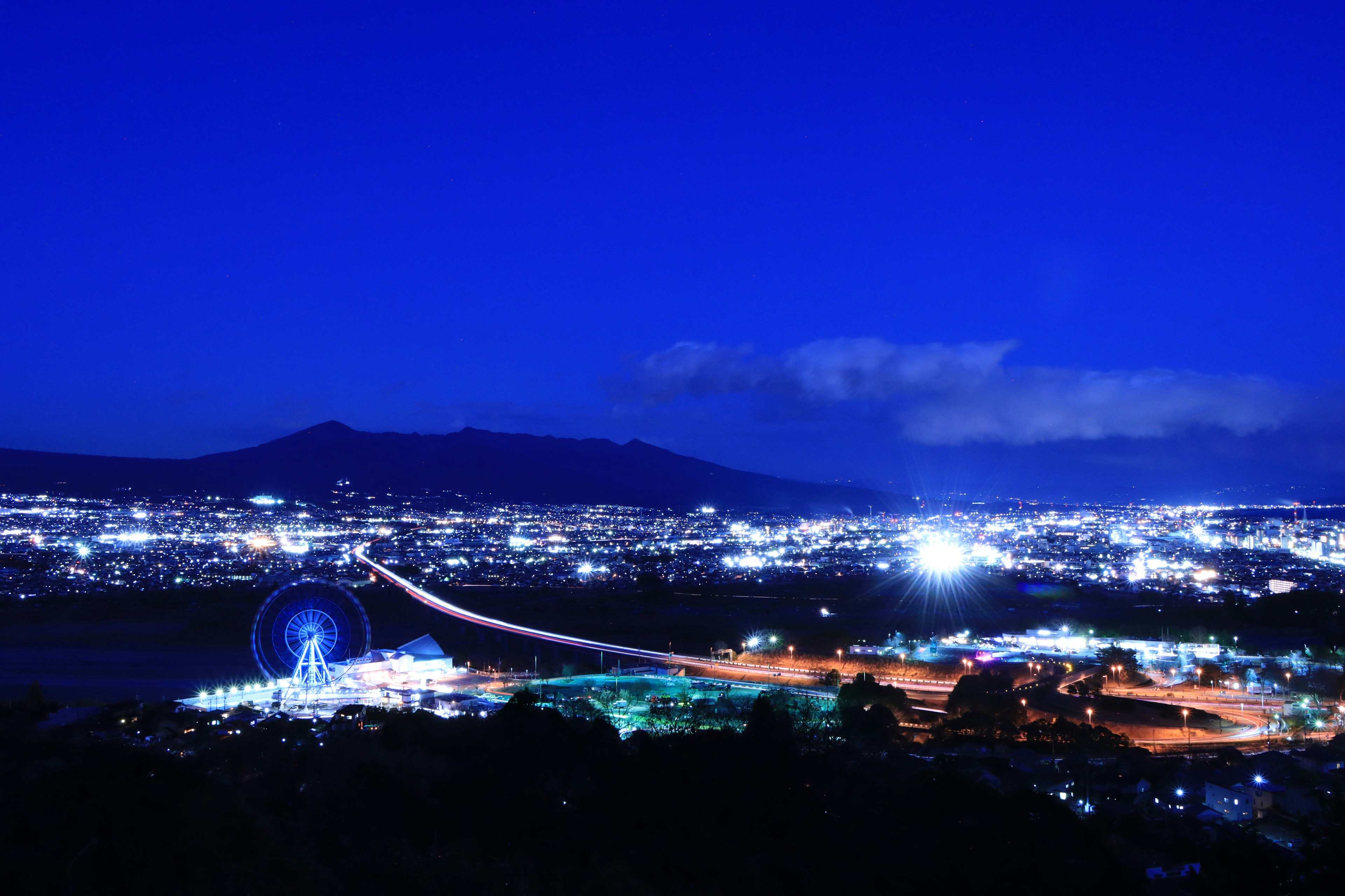 ทิวทัศน์เมืองที่มีชีวิตชีวาในเวลากลางคืนที่มีชิงช้าสวรรค์และสะพาน