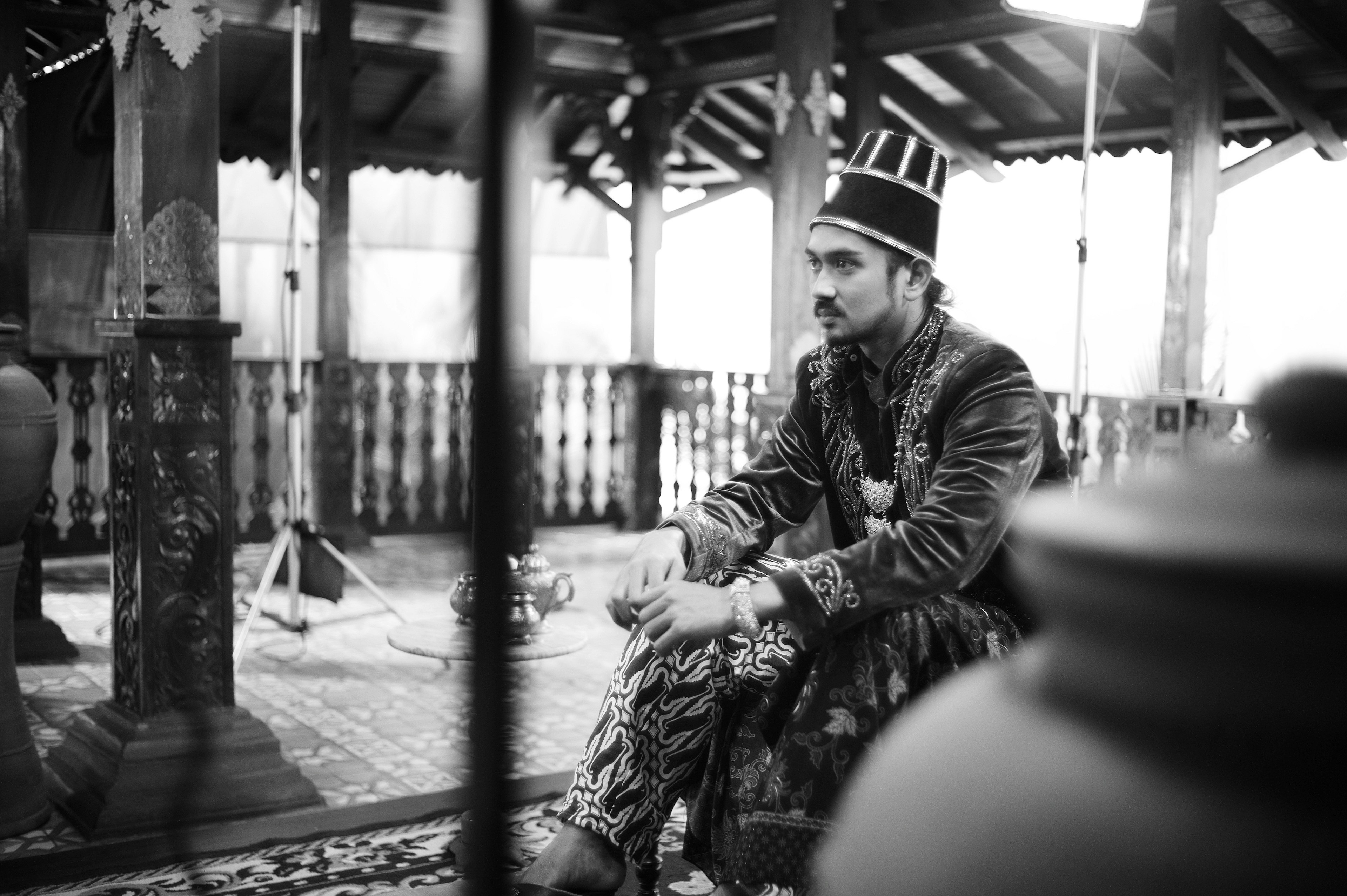 Un hombre en atuendo tradicional sentado en interiores en blanco y negro