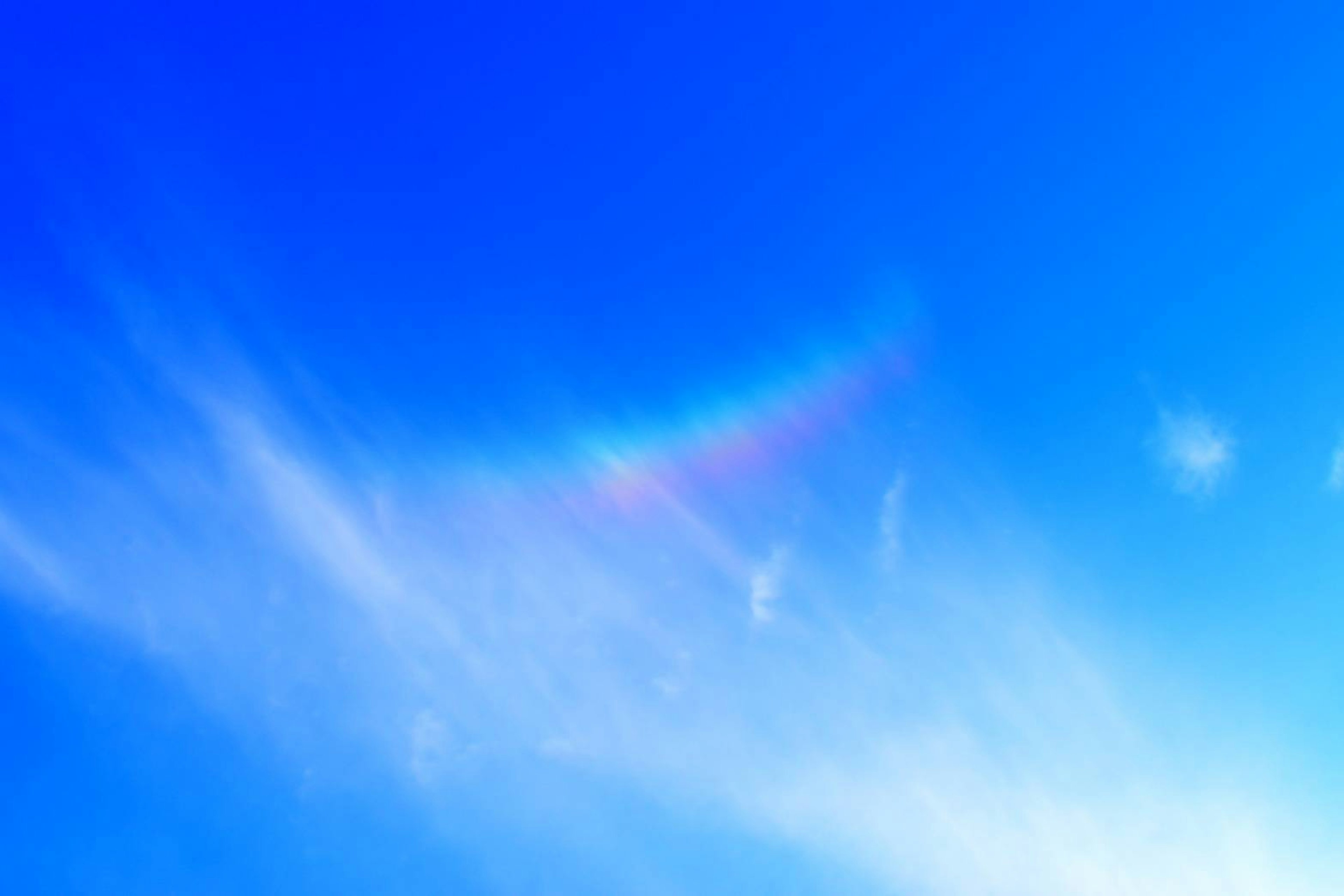 Bright blue sky with wispy clouds and a hint of rainbow colors