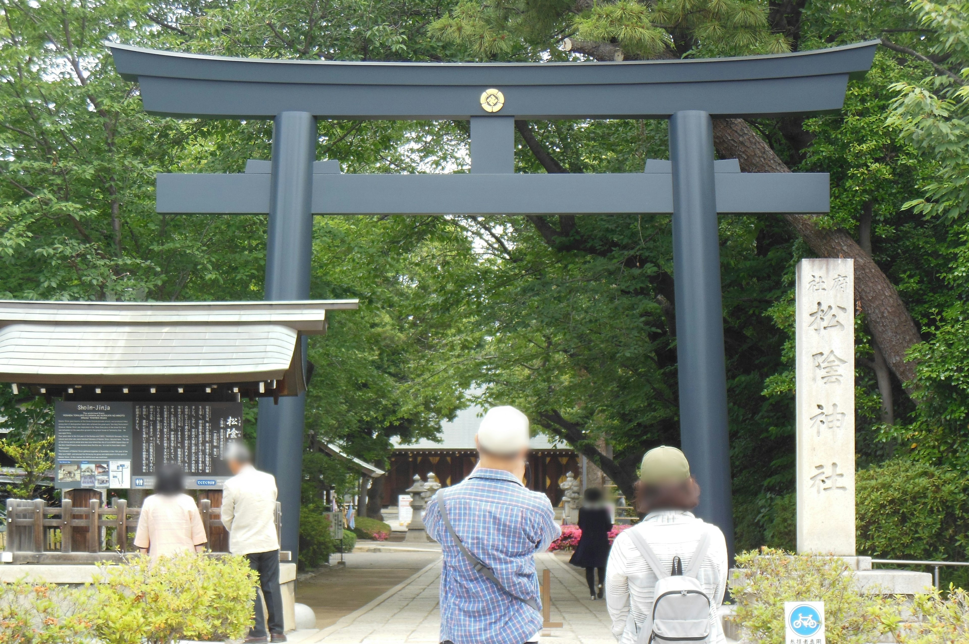 People walking towards a black torii gate and shrine path