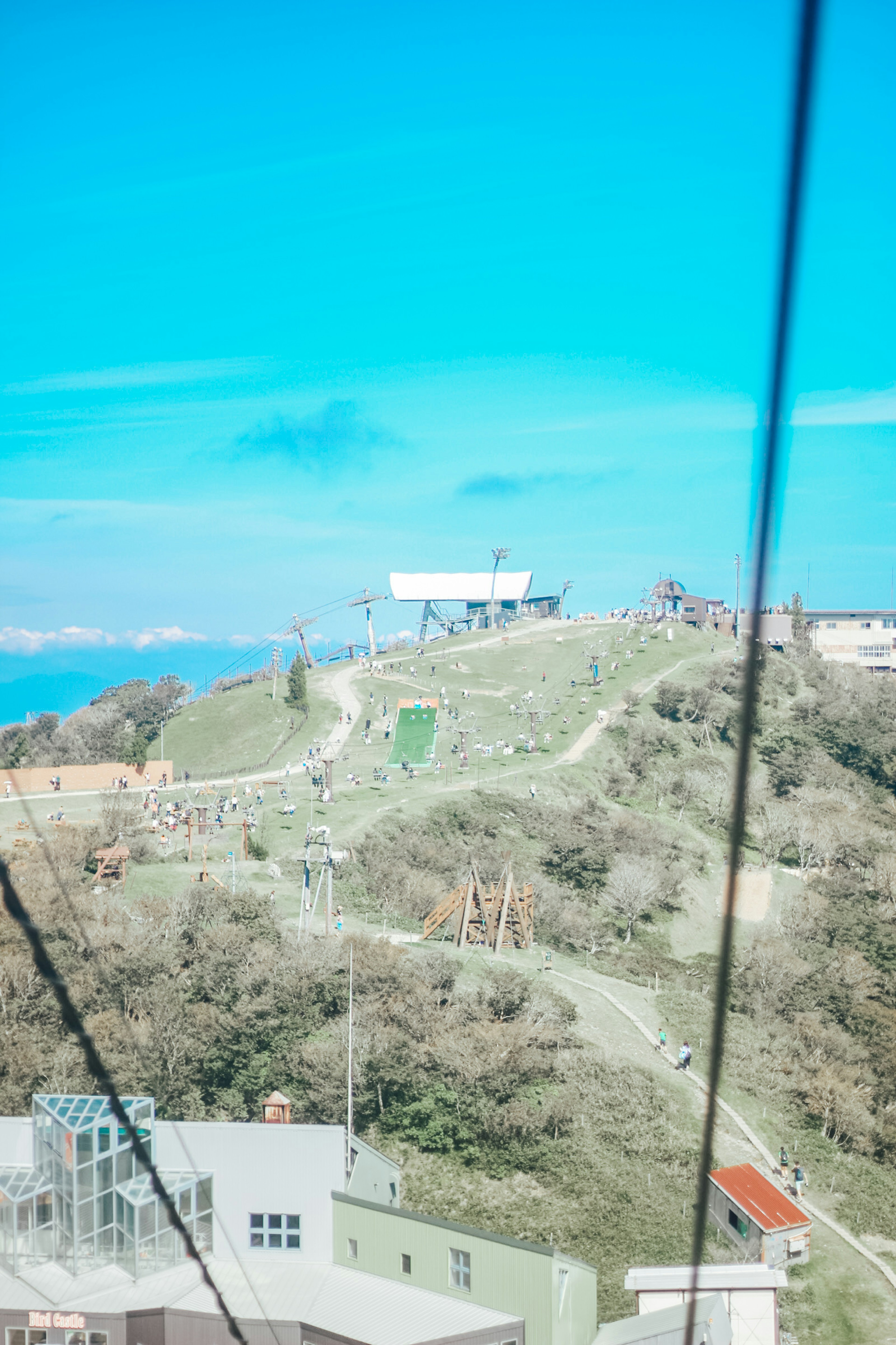 A landscape under a blue sky featuring a white building on a hill, with green slopes and playground equipment