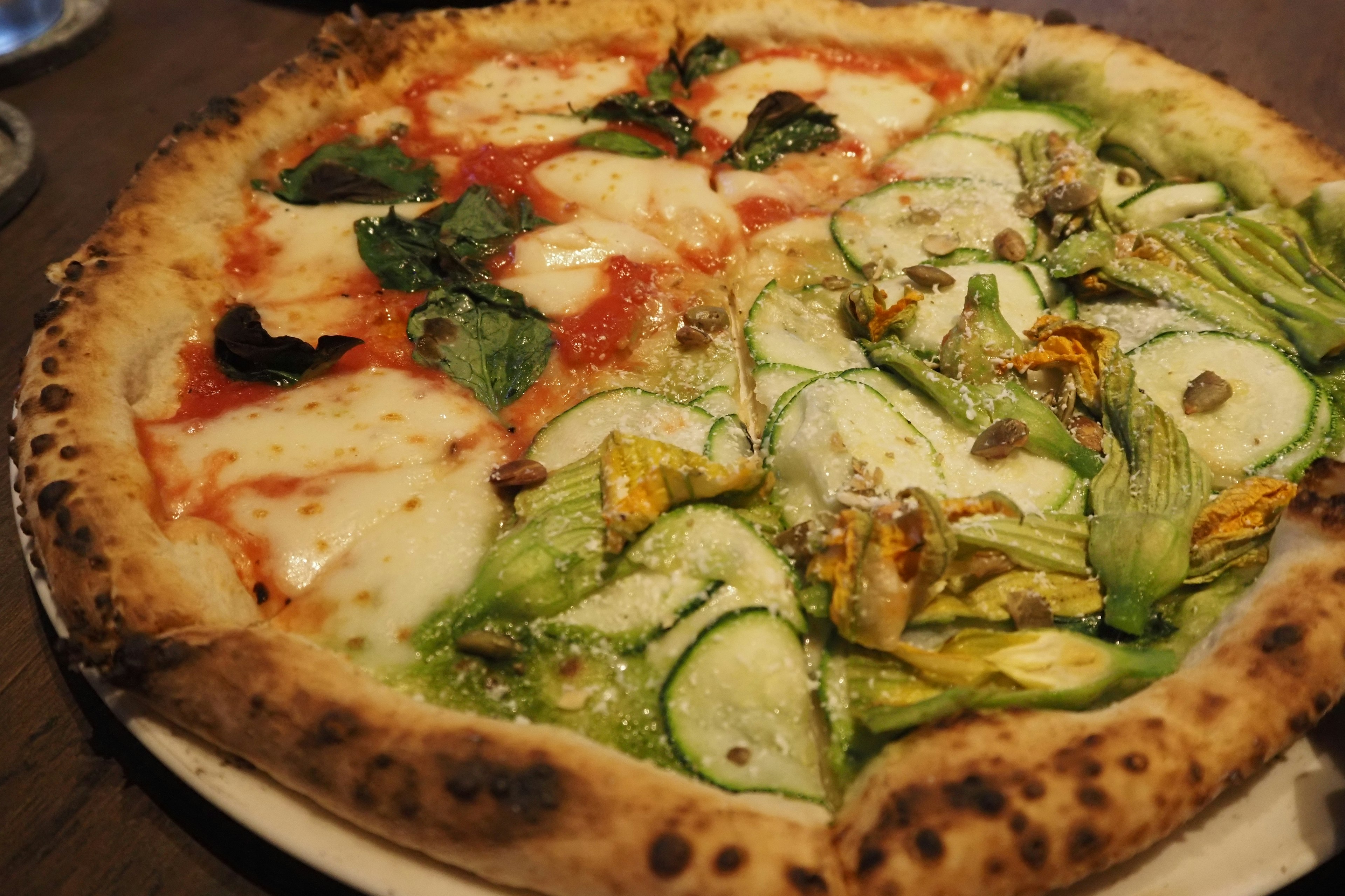 Half tomato sauce and mozzarella cheese pizza with basil and half zucchini and flower topped pizza