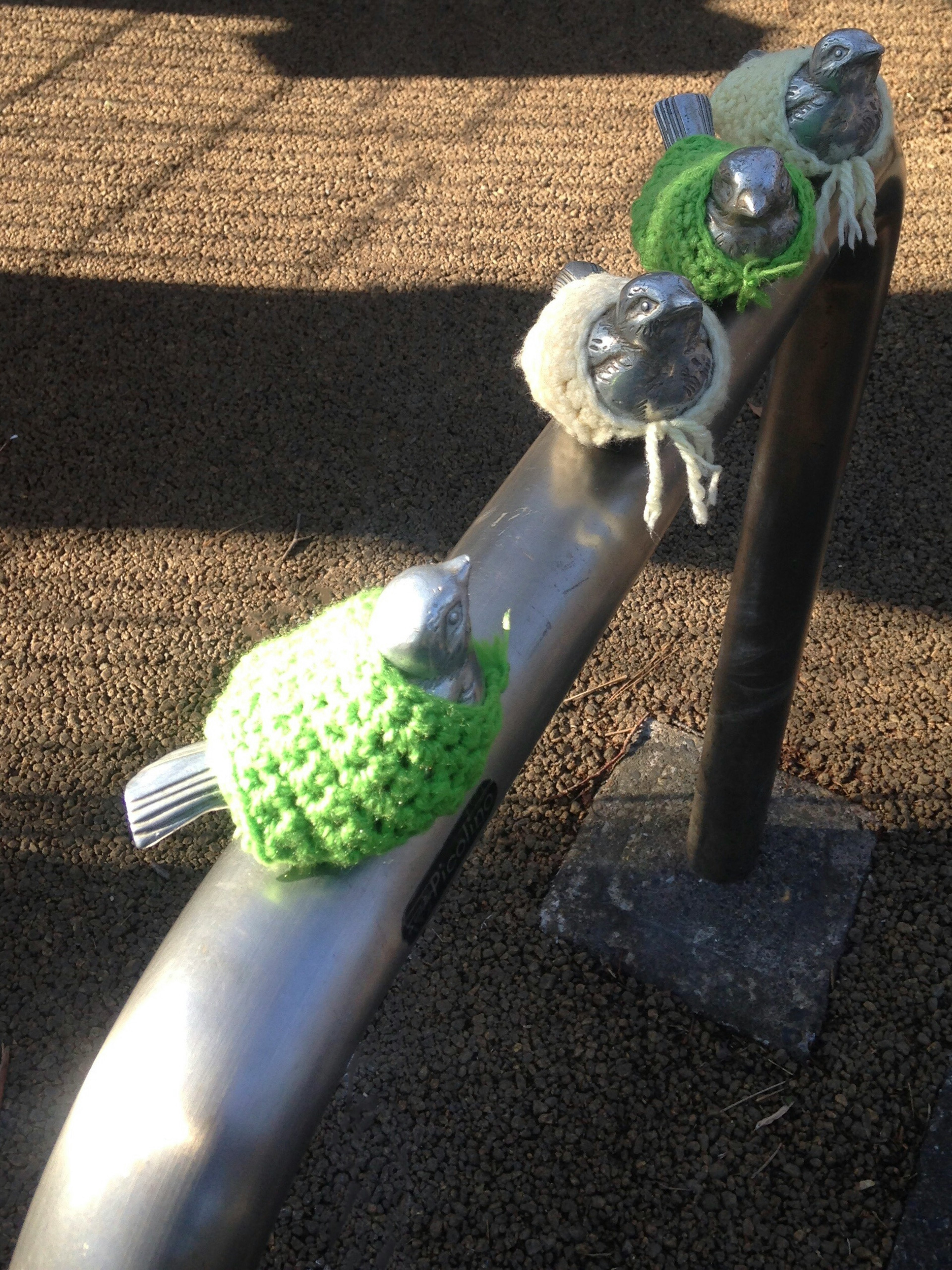 Colorful knitted birds wearing hats on a metal railing