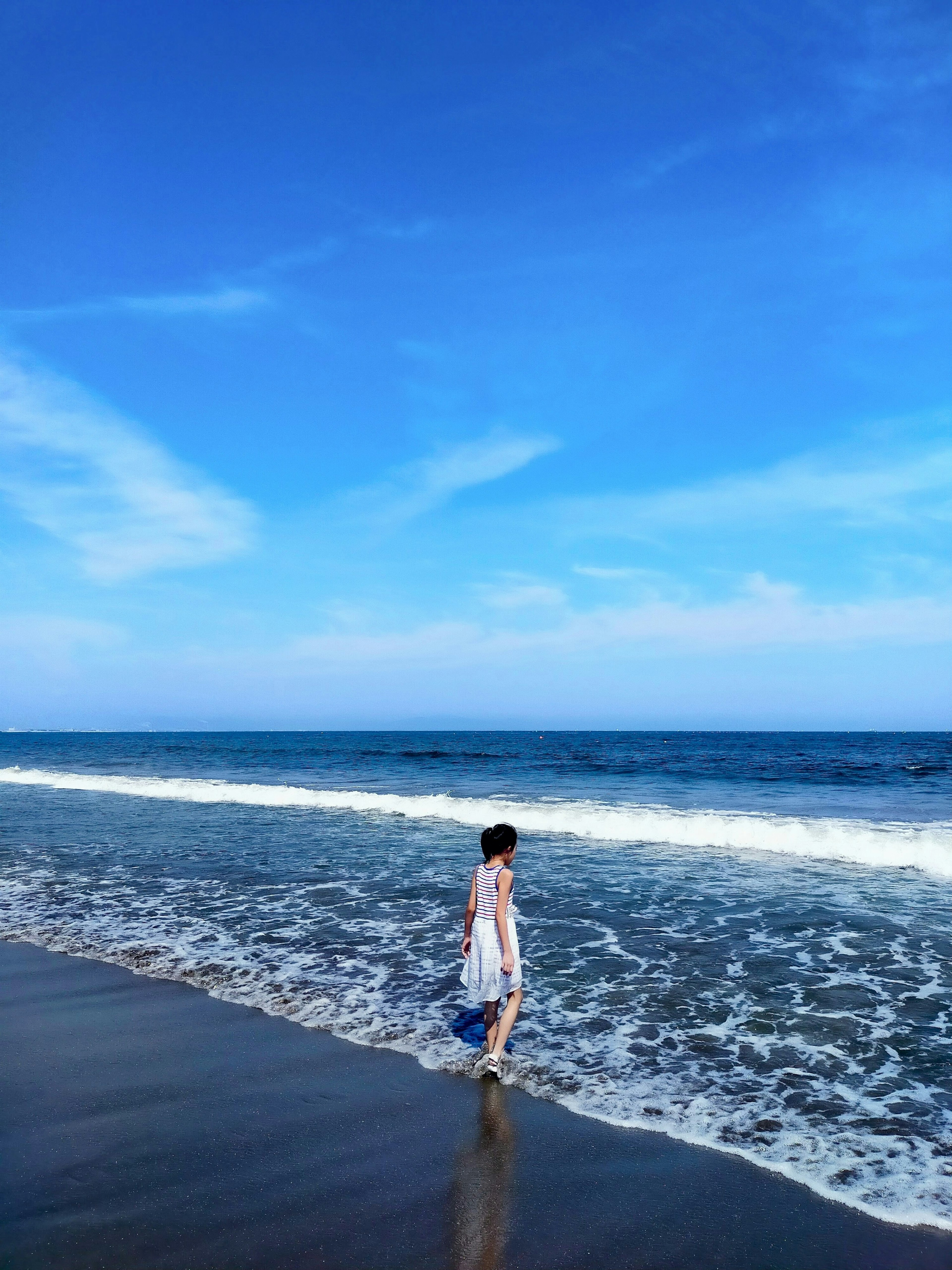 Mujer caminando por una hermosa playa con cielo azul y olas