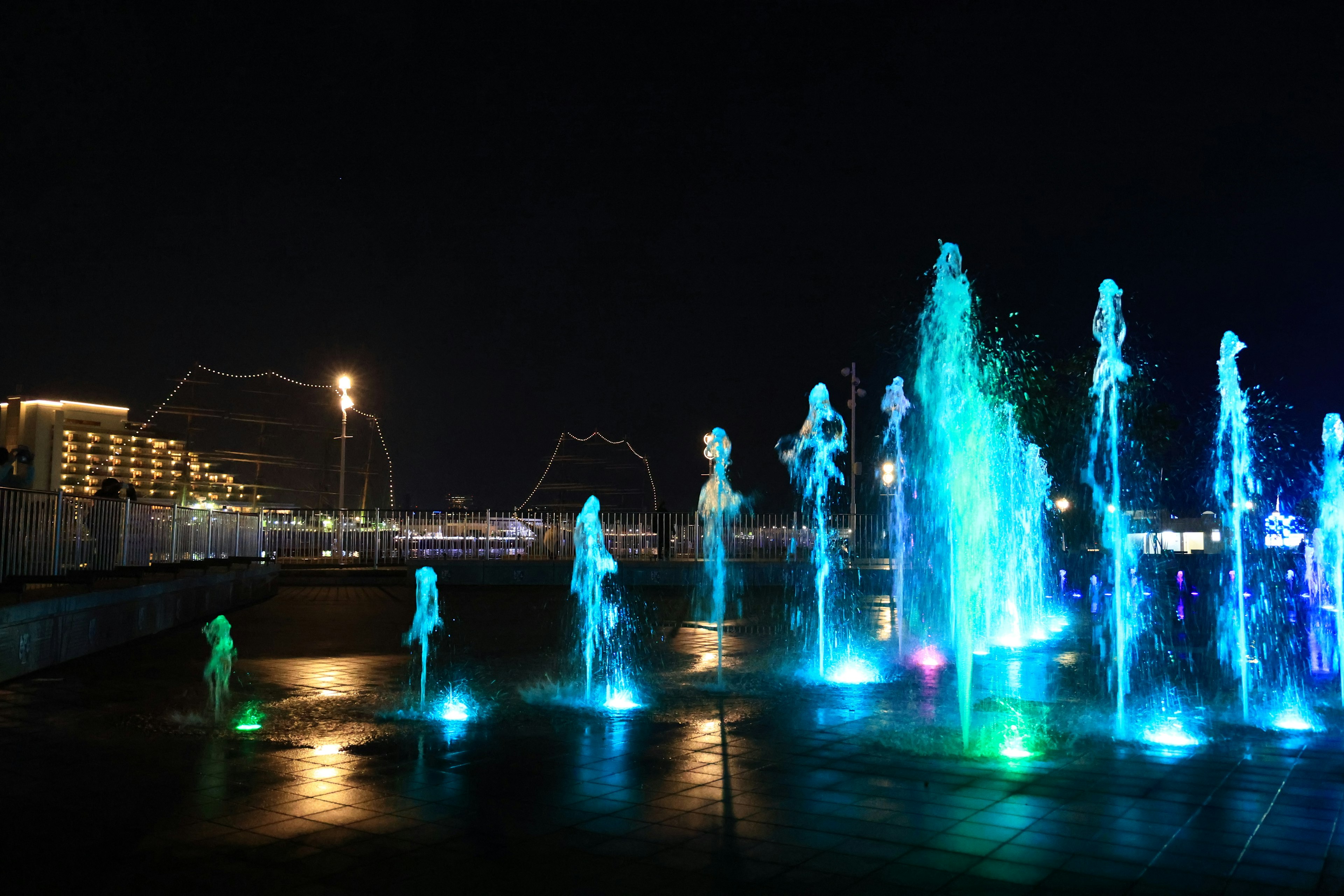 Nighttime fountain display with blue and green lights illuminating the water jets