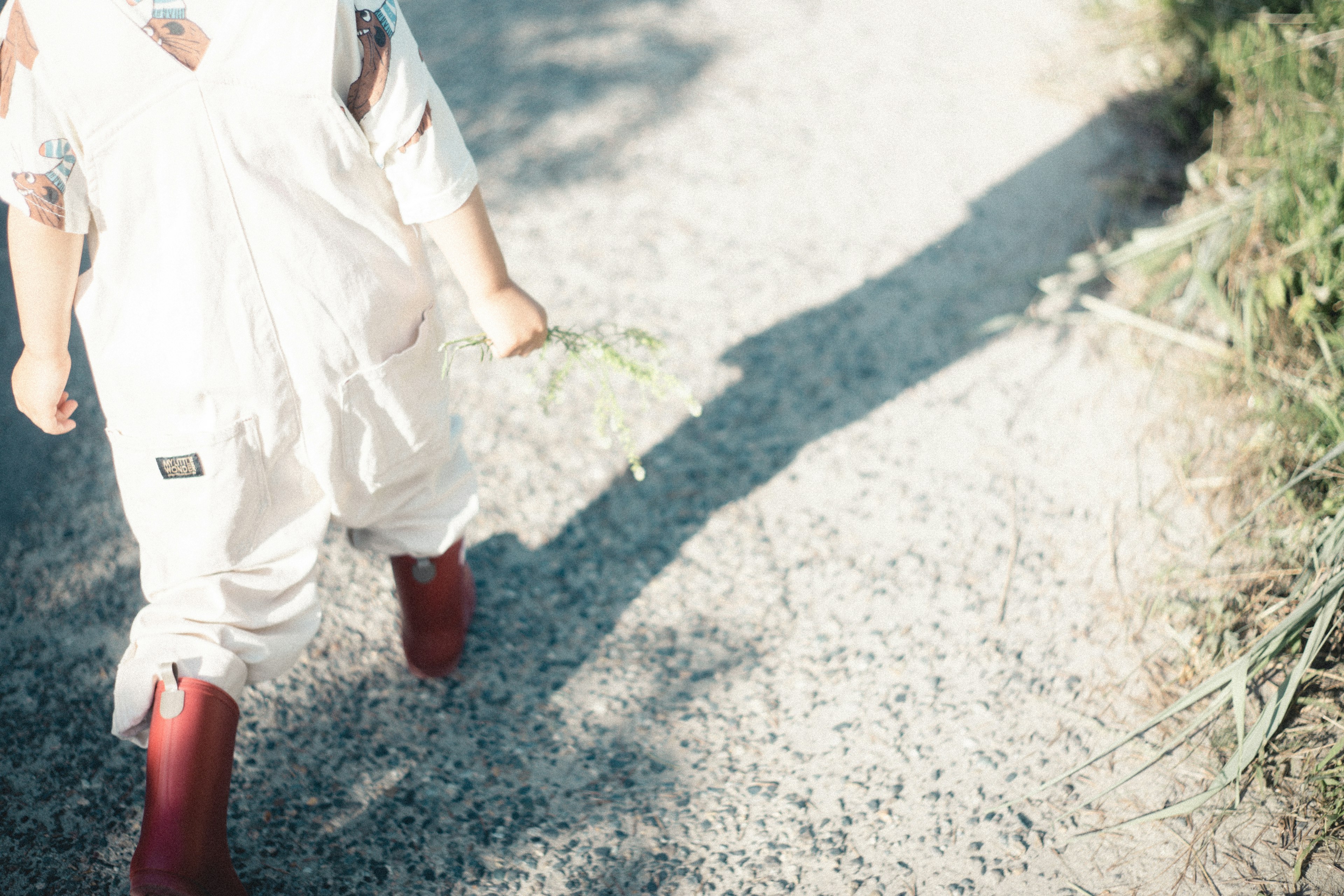 Bambino che cammina su un sentiero di ghiaia con stivali rossi e abbigliamento bianco