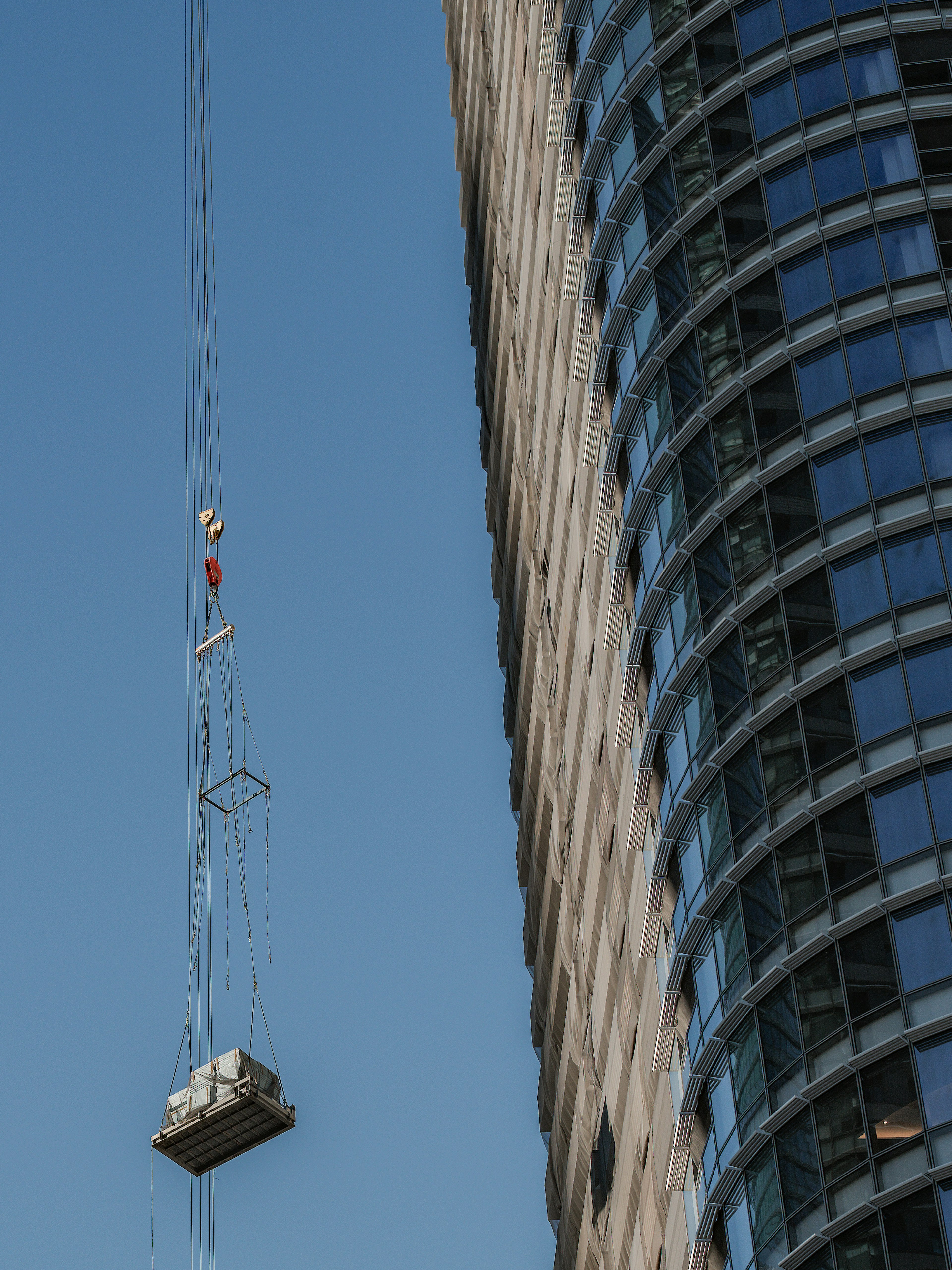 Una gru per la pulizia delle finestre sospesa contro un cielo blu chiaro accanto a un edificio alto