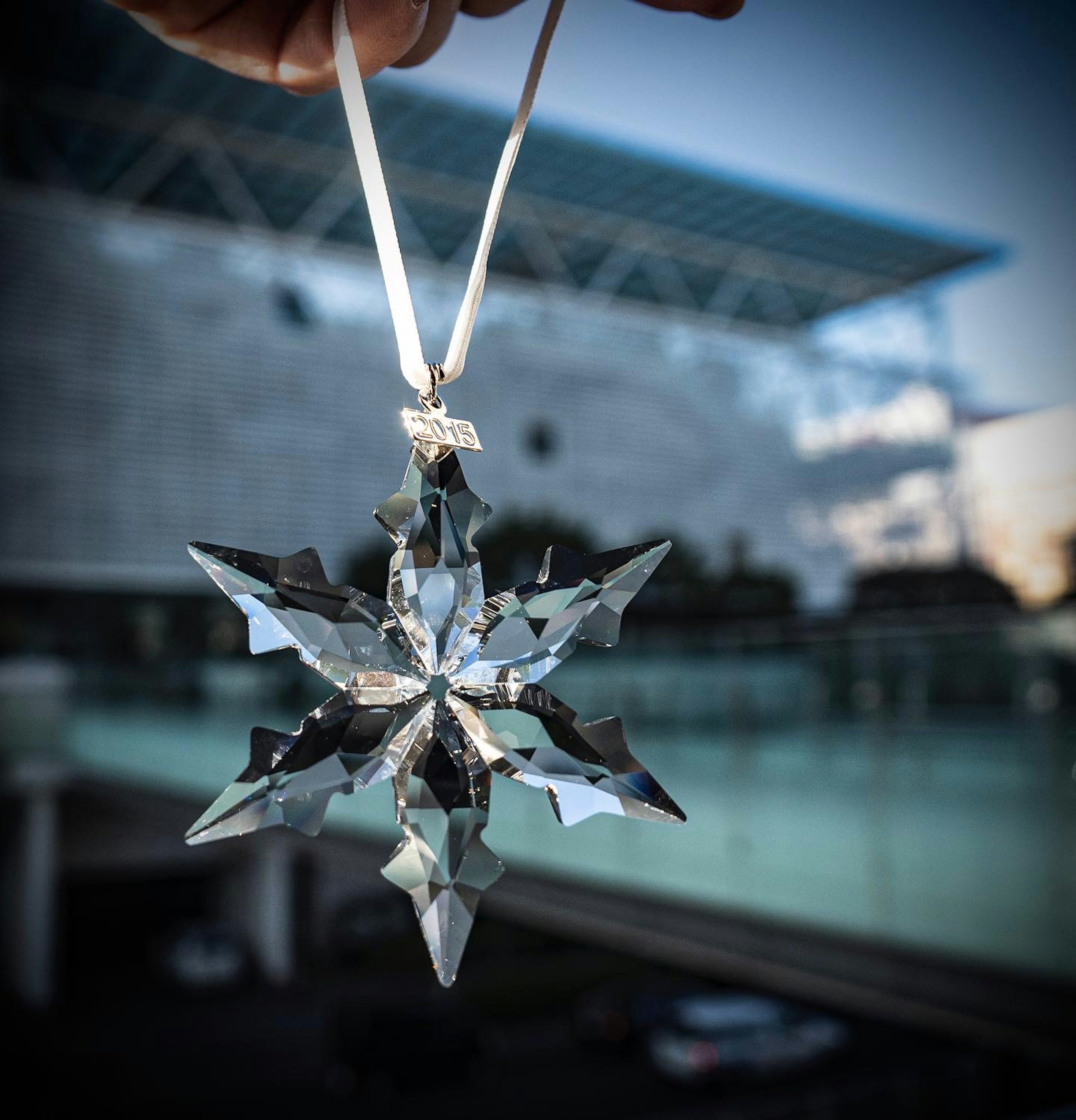 Crystal snowflake ornament held in hand with a modern building in the background