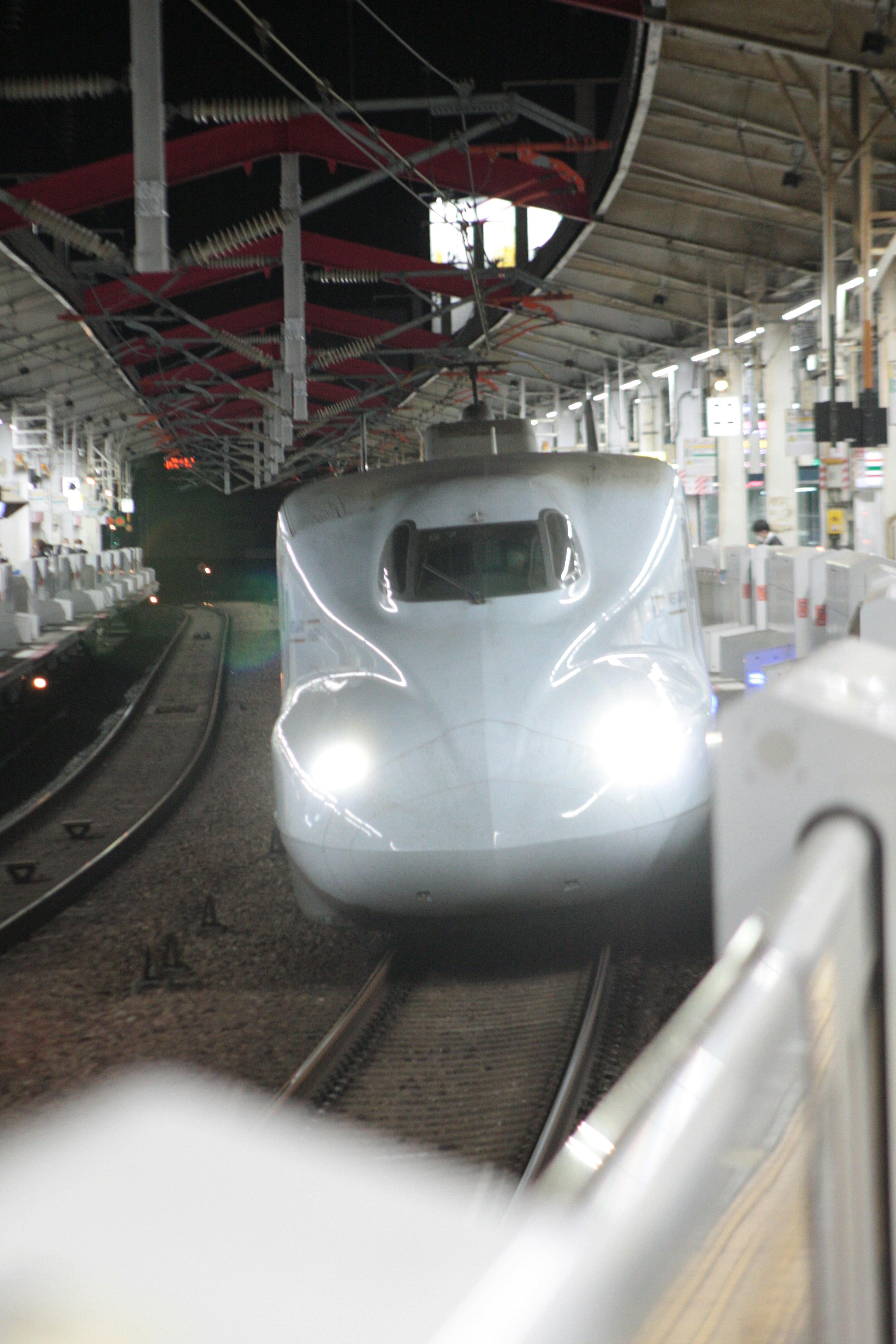 Shinkansen arriving at a station with bright headlights at night