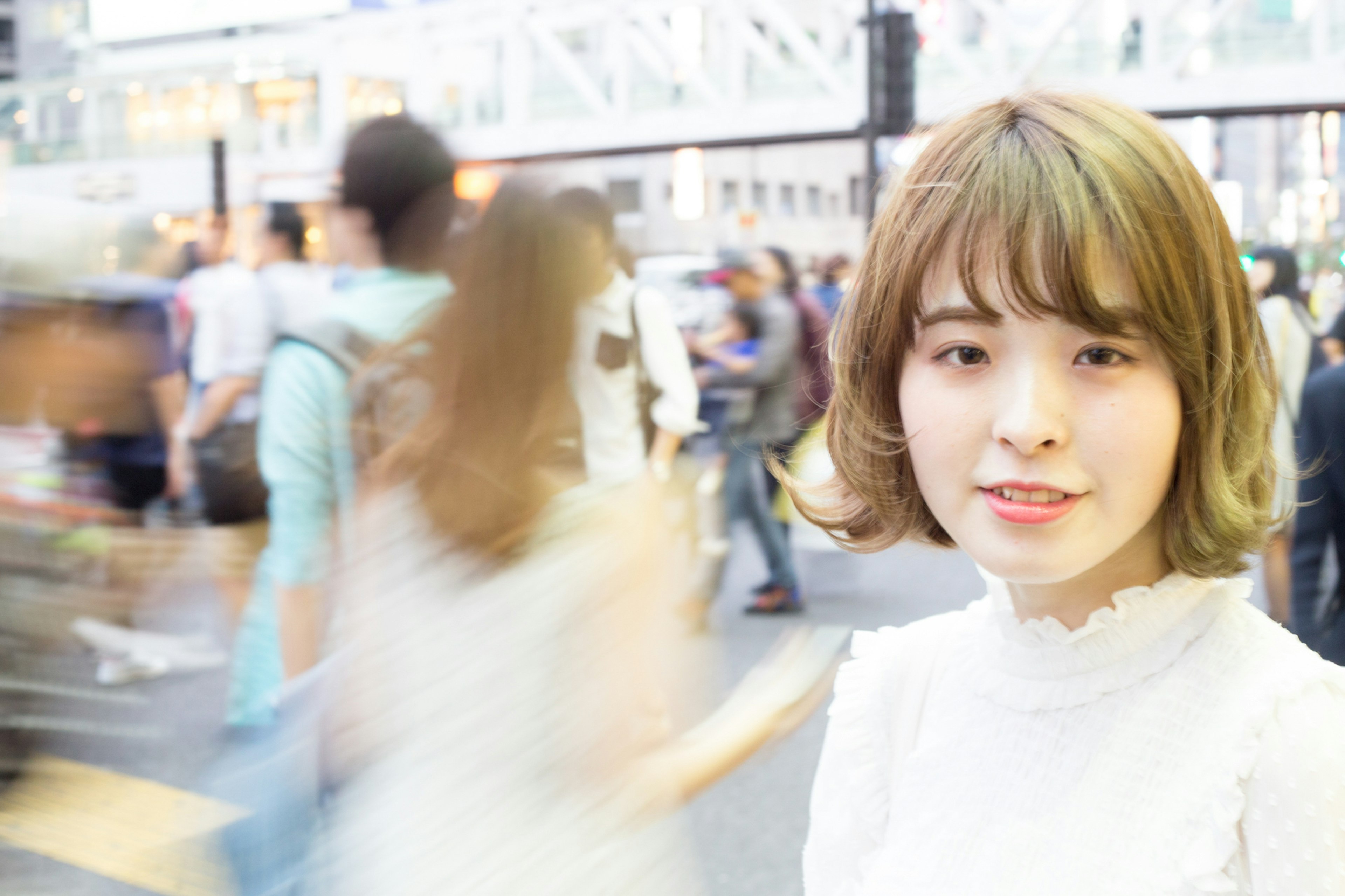 A smiling woman in a white outfit amidst a bustling crowd urban setting