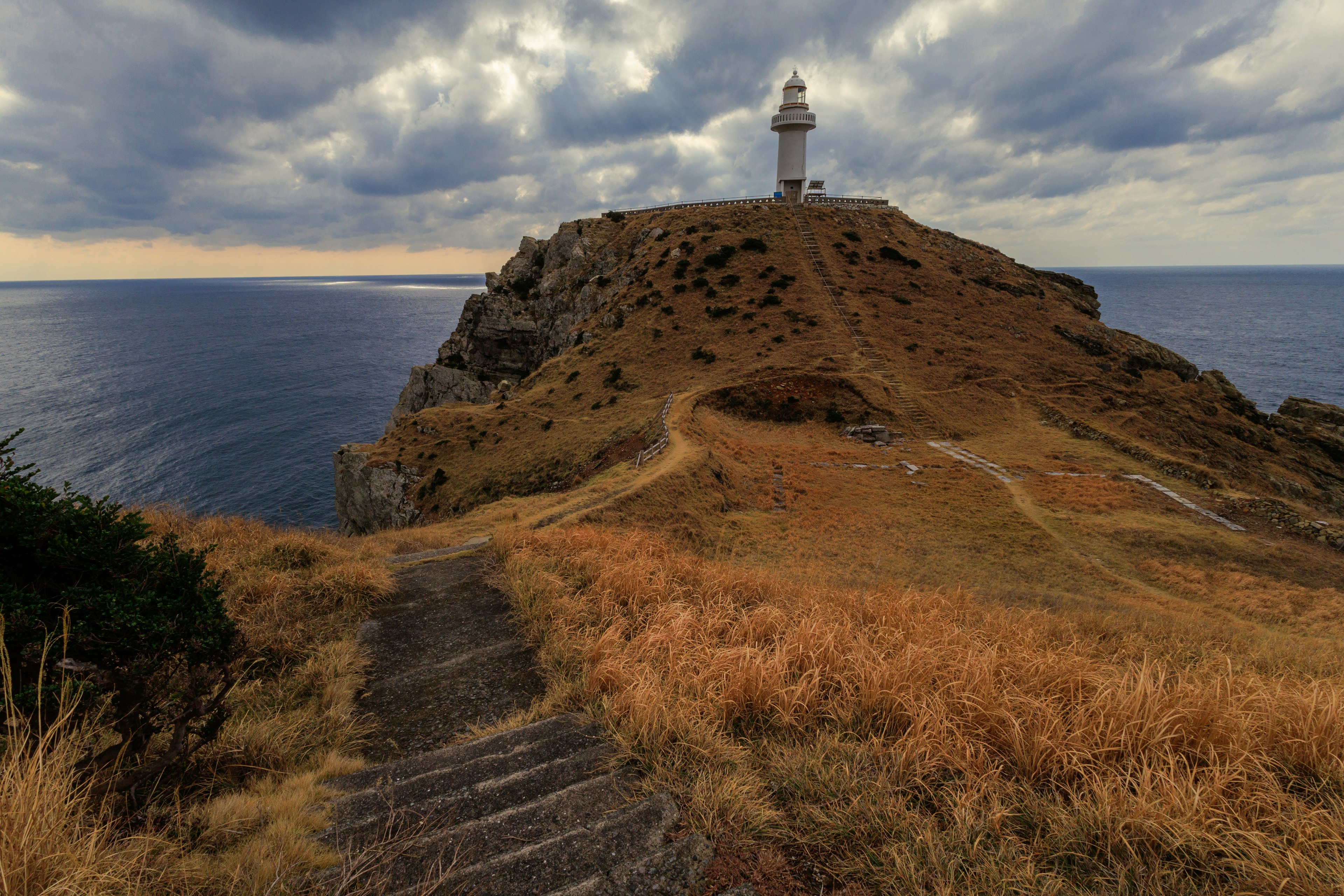 Paesaggio costiero con un faro su una collina sentieri erbosi e terreno roccioso