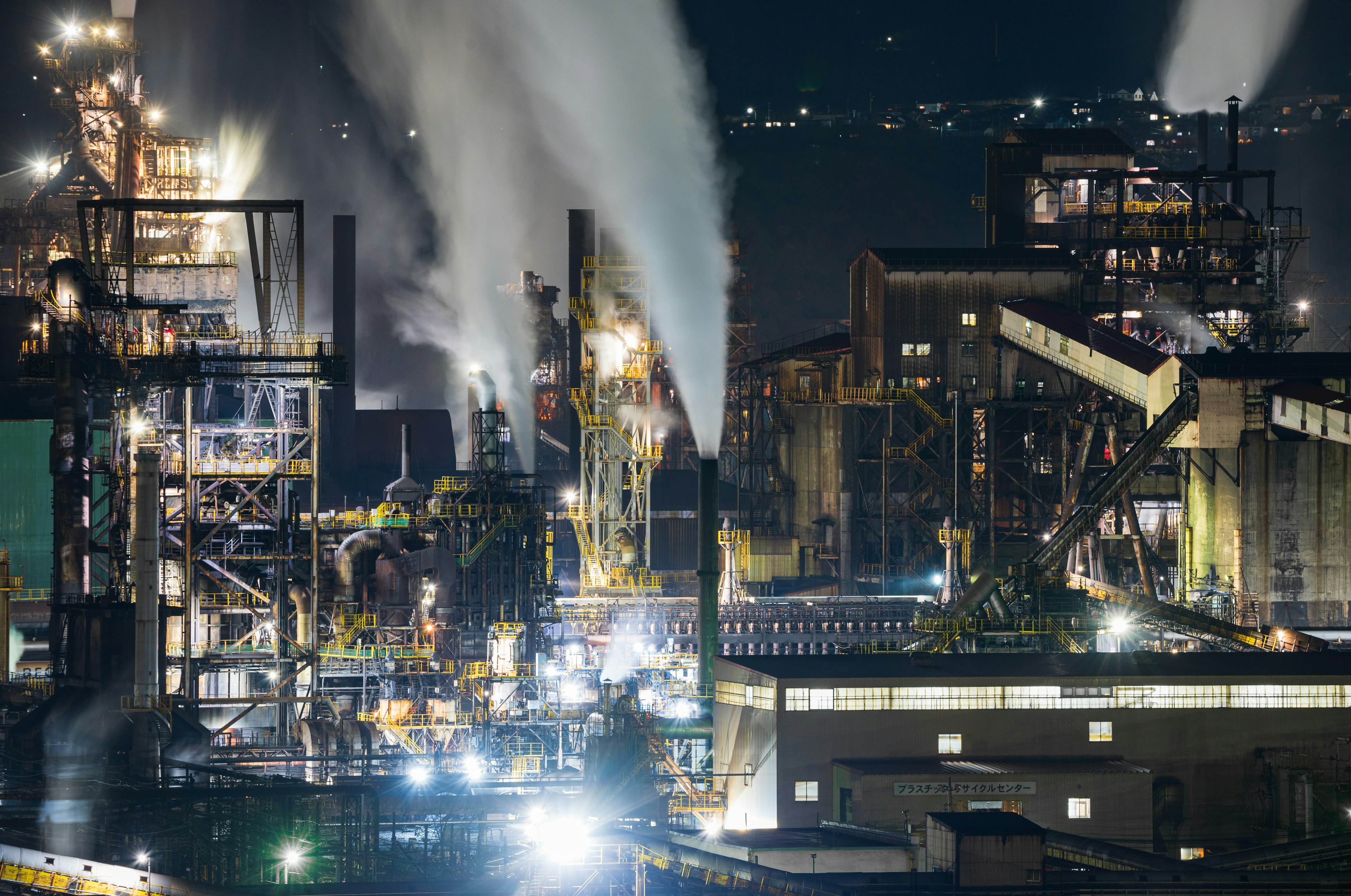 Industriekomplex bei Nacht mit Rauch, der aus Schornsteinen aufsteigt