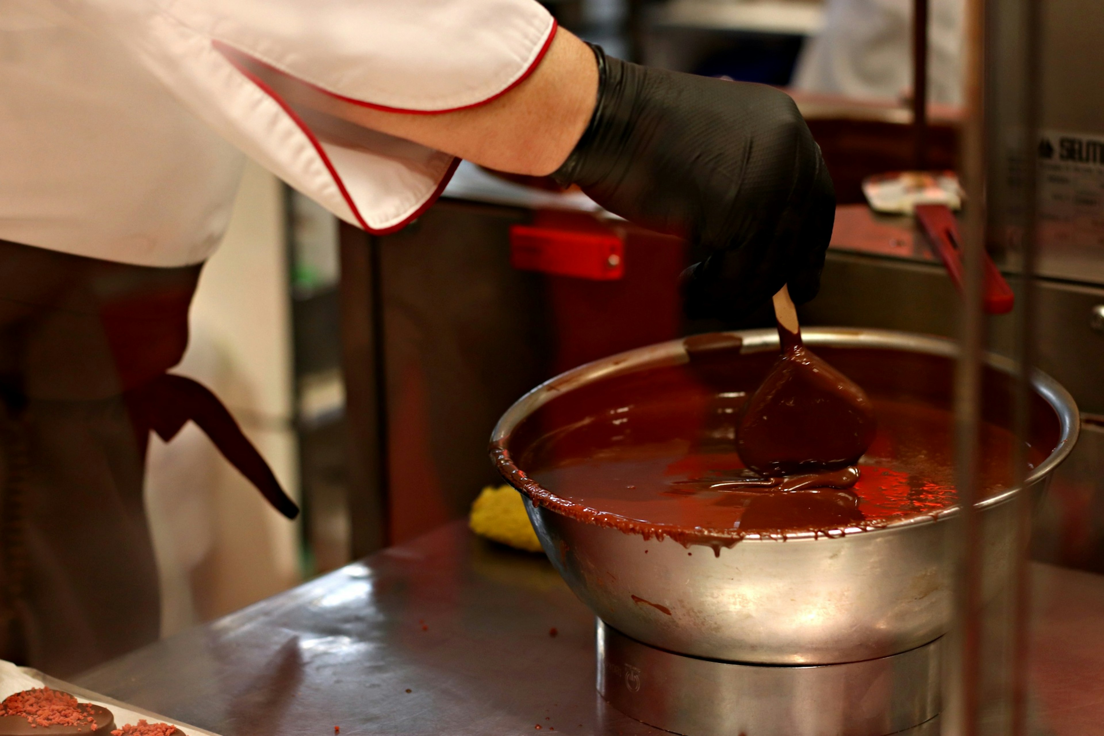 Chef con guantes negros mezclando chocolate en un tazón grande