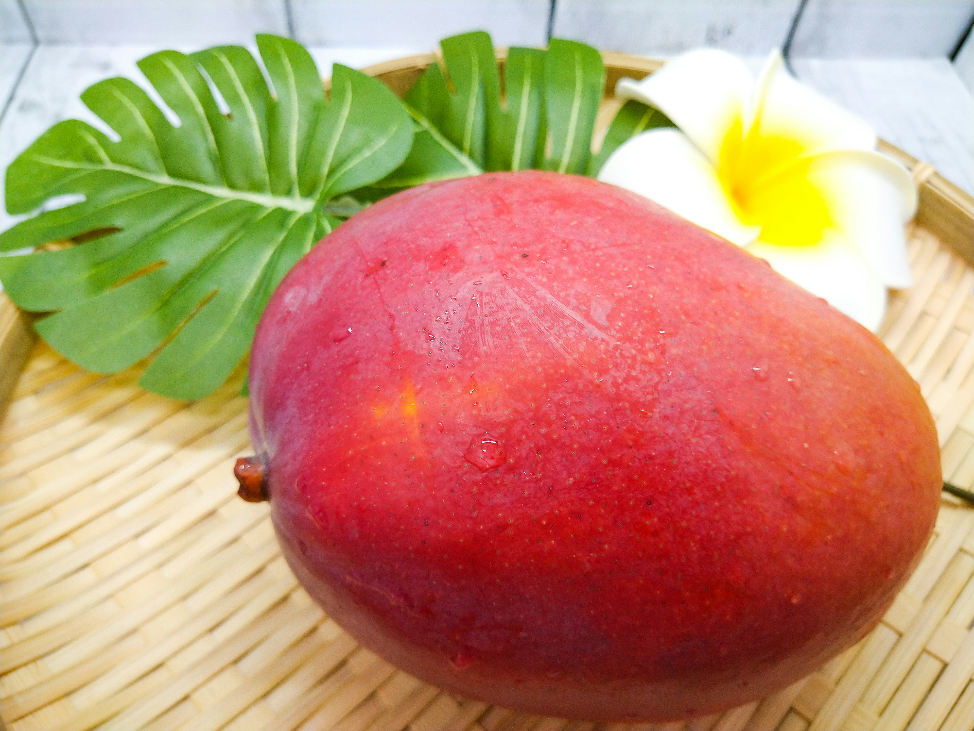 Vibrant red mango with green leaves and a white flower arrangement