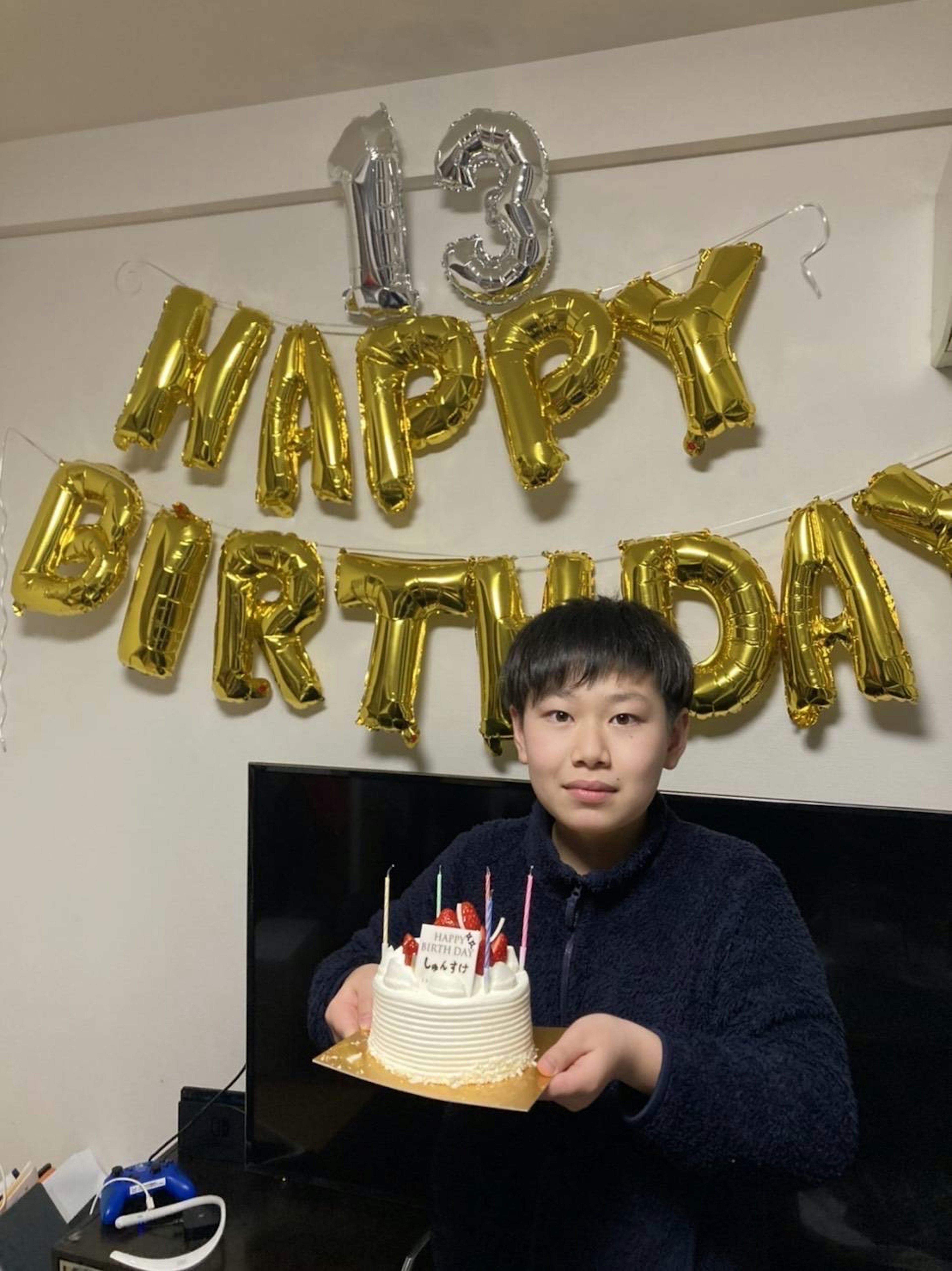 13歳の誕生日を祝う少年がケーキを持っている部屋の中