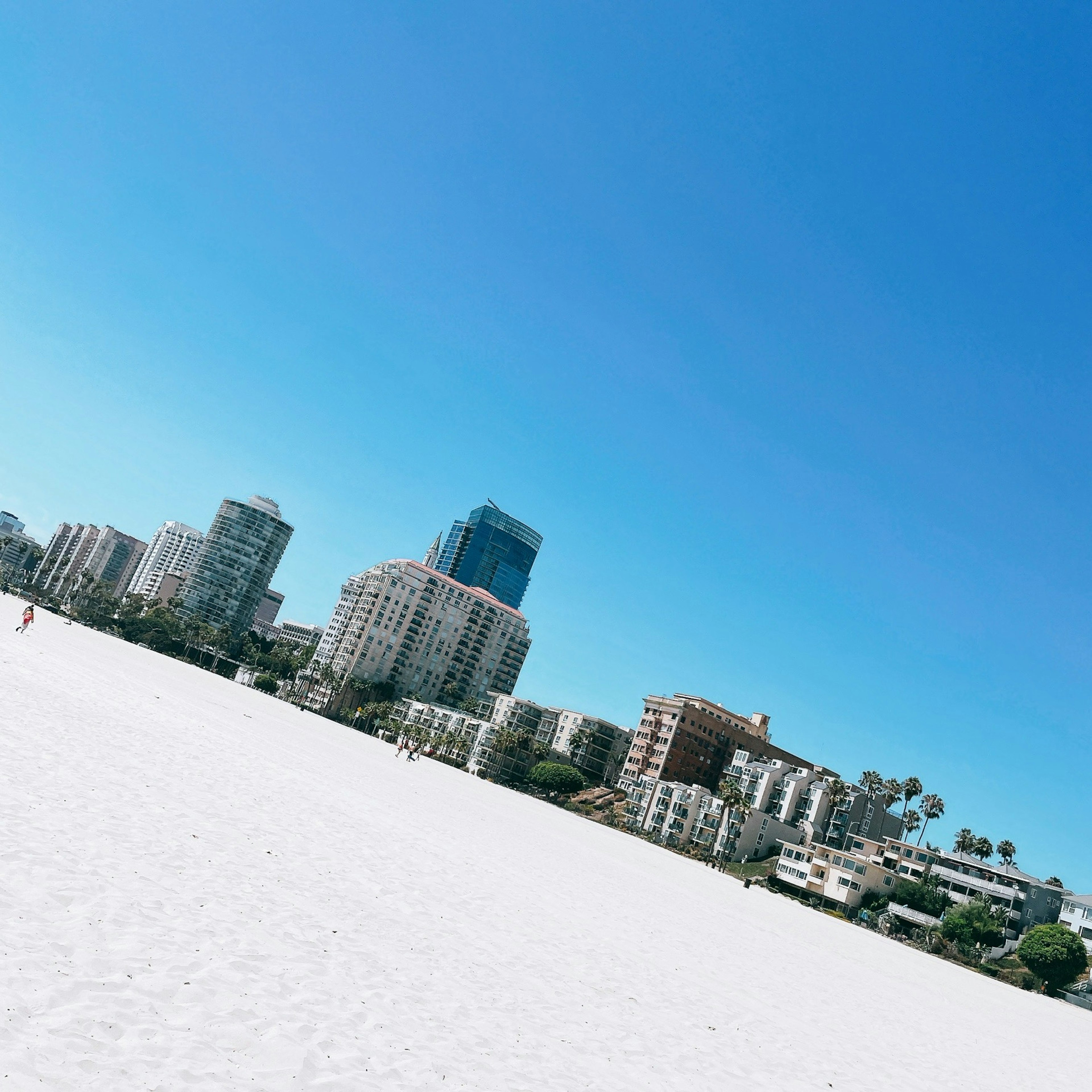 Una vista di una spiaggia di sabbia bianca con alti edifici sotto un cielo blu chiaro