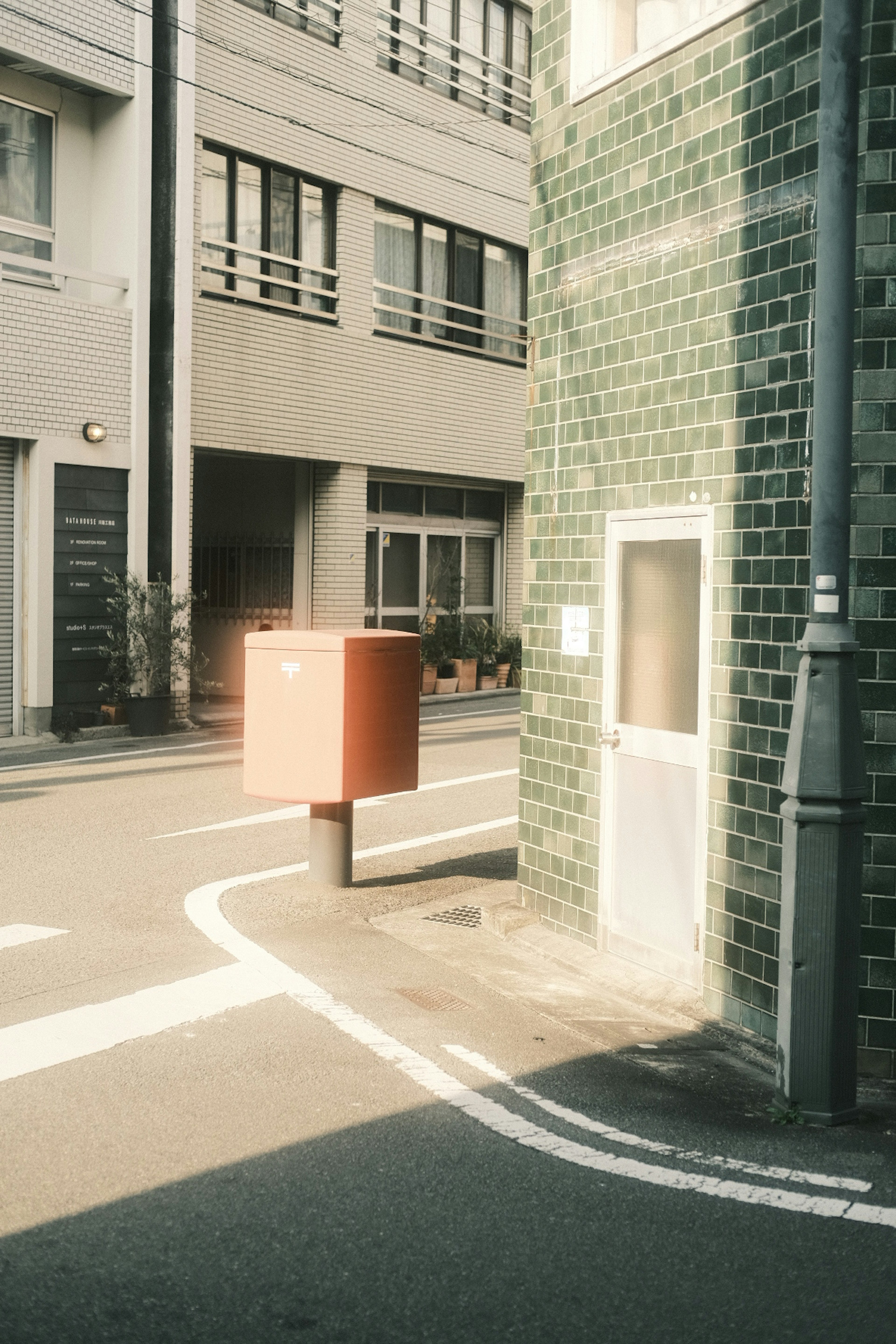 Straßenecke mit einem orangefarbenen Briefkasten und einem gefliesten Gebäude