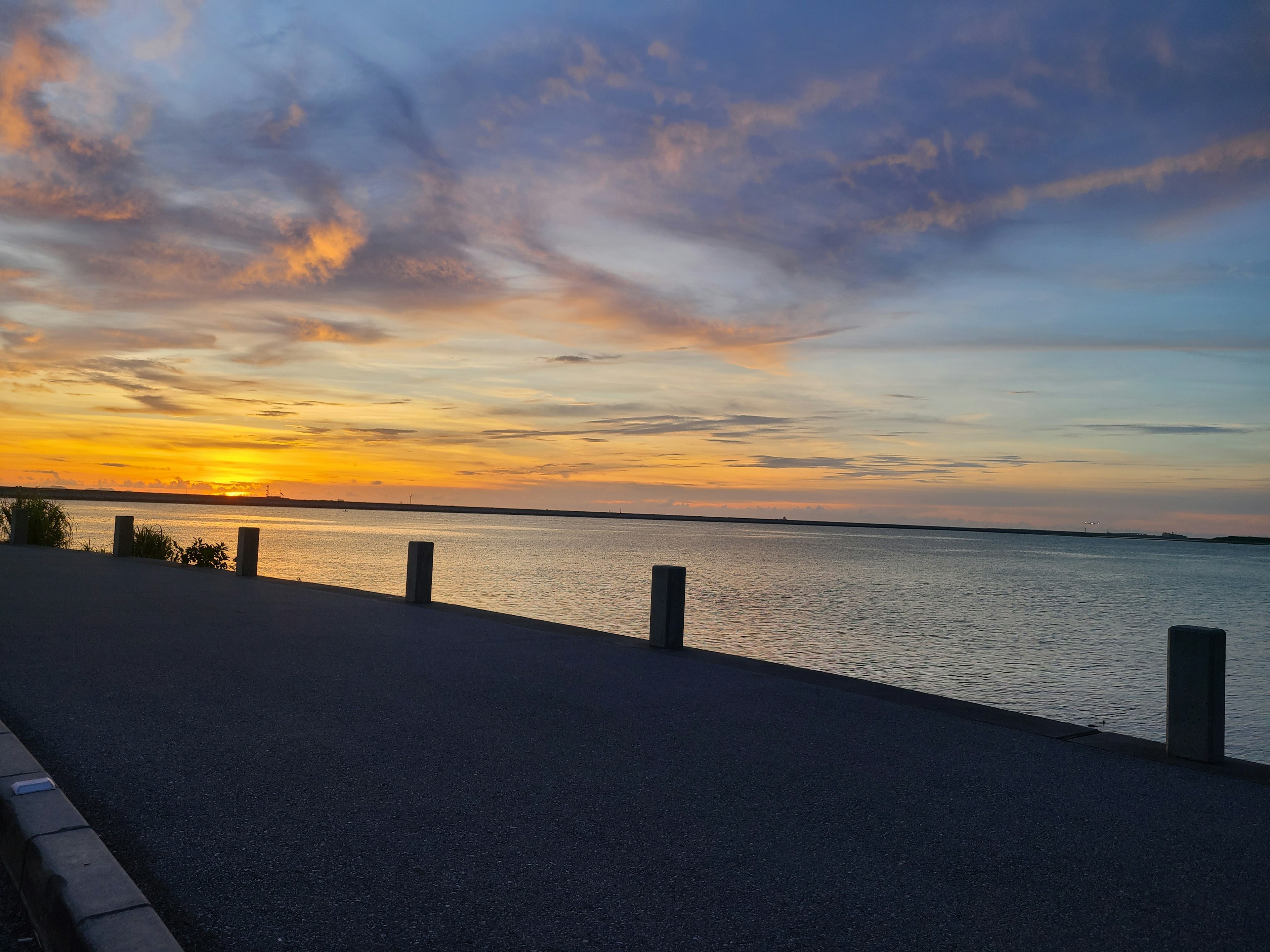 Vista escénica de una puesta de sol sobre el agua con un camino pavimentado