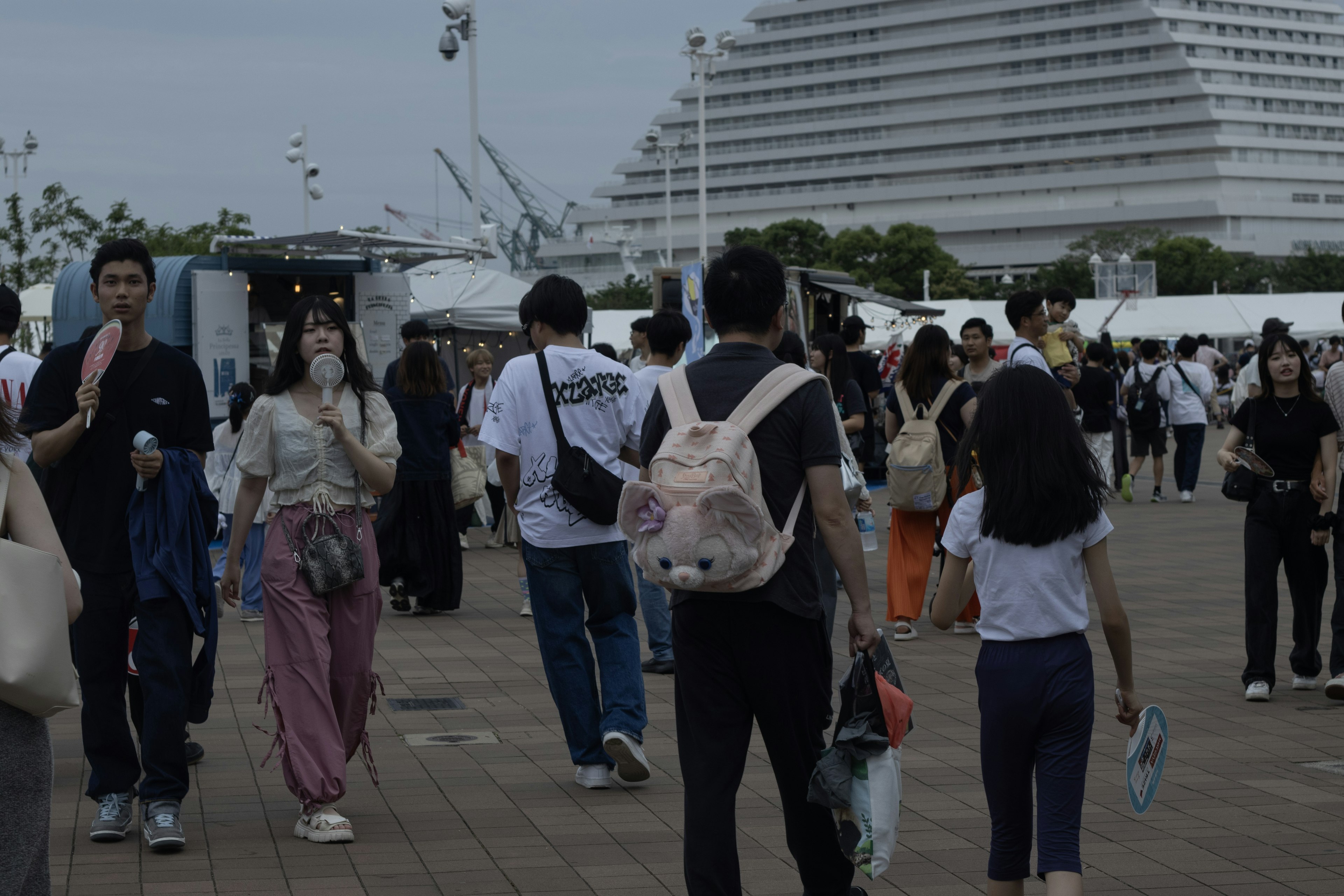 Crowd of people at a lively event featuring a large building and food stalls in the background