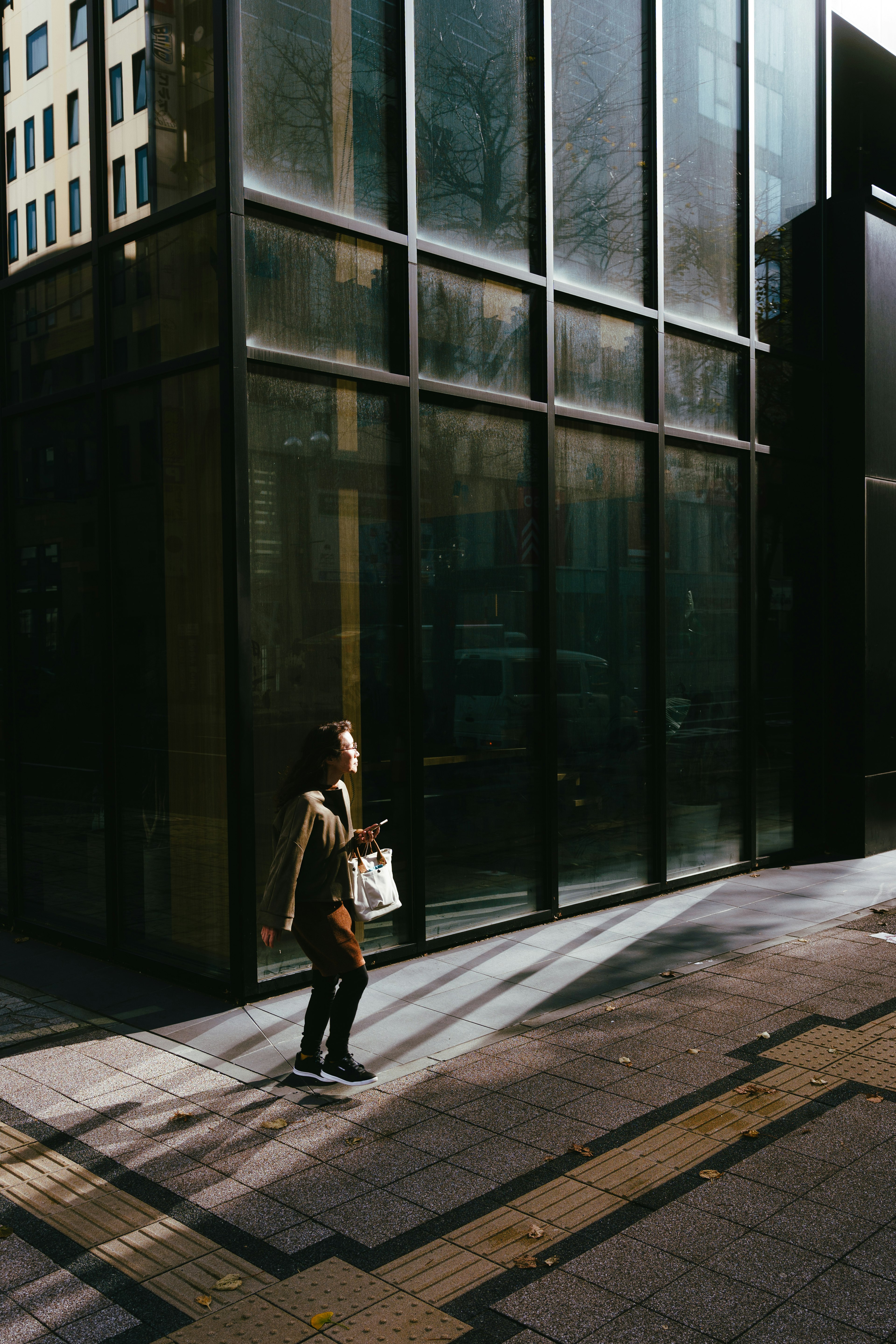 Una mujer caminando frente a un edificio de vidrio con sombras