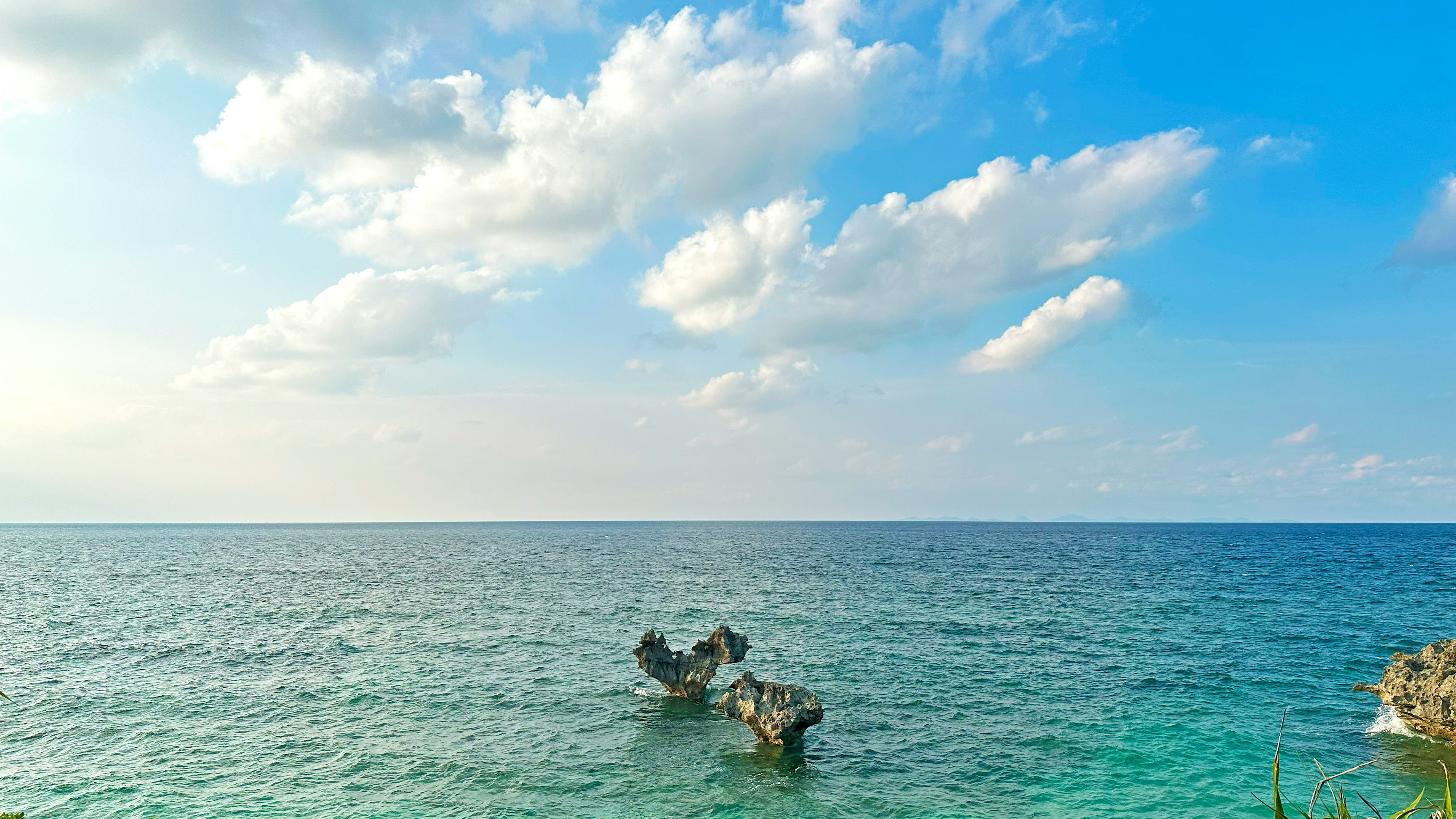 青い海と空に浮かぶ雲が広がる風景に、古いボートが浮かんでいる