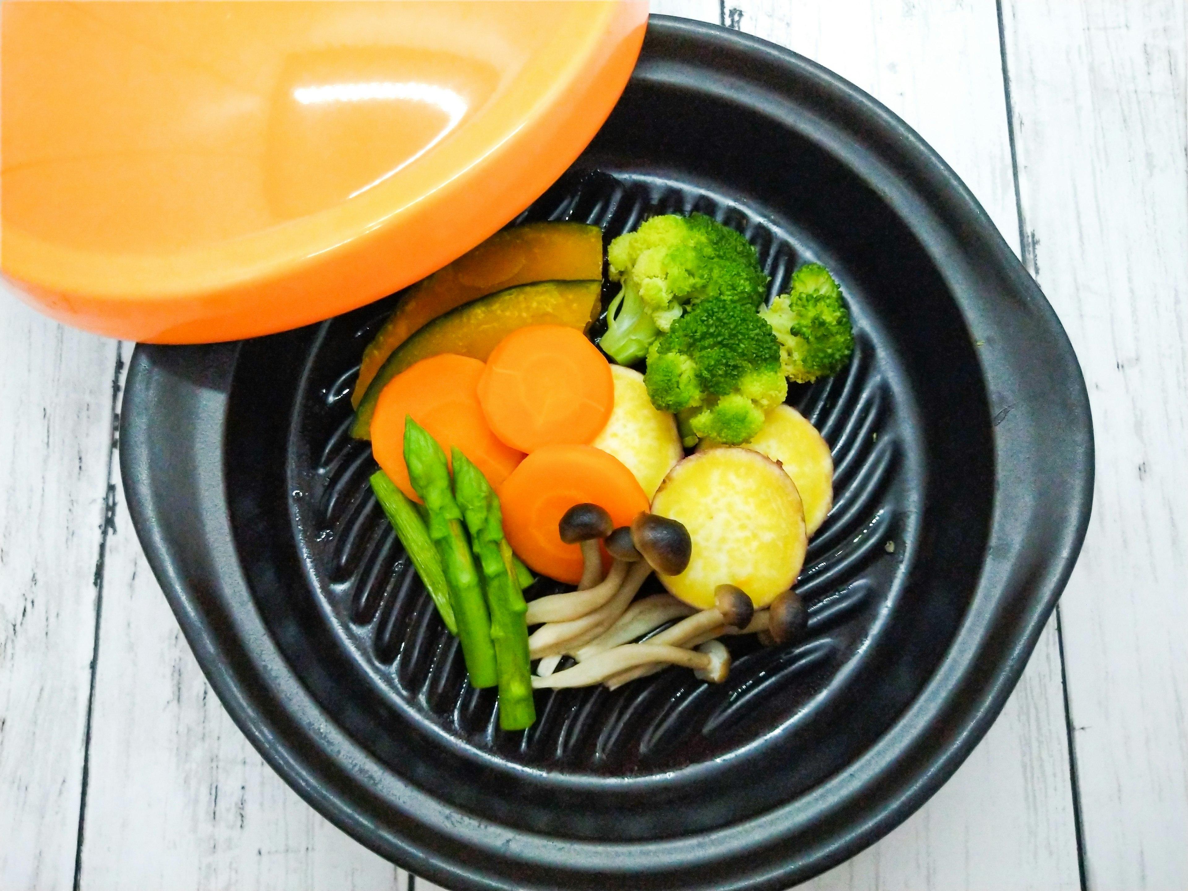 Assortiment de légumes dans une casserole noire avec un couvercle orange comprenant du brocoli des carottes et des asperges