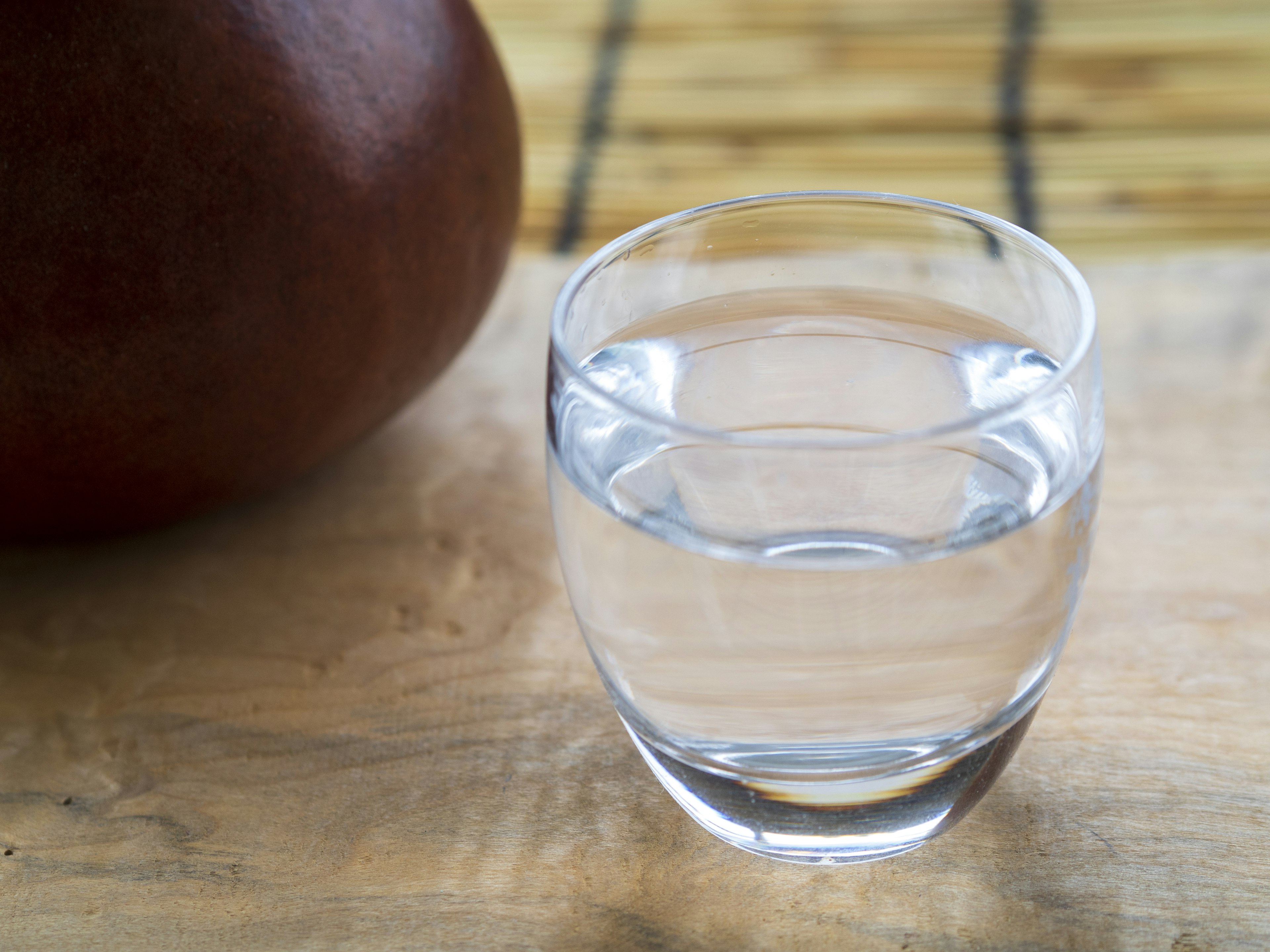 A clear glass of water next to a brown pot on a wooden table