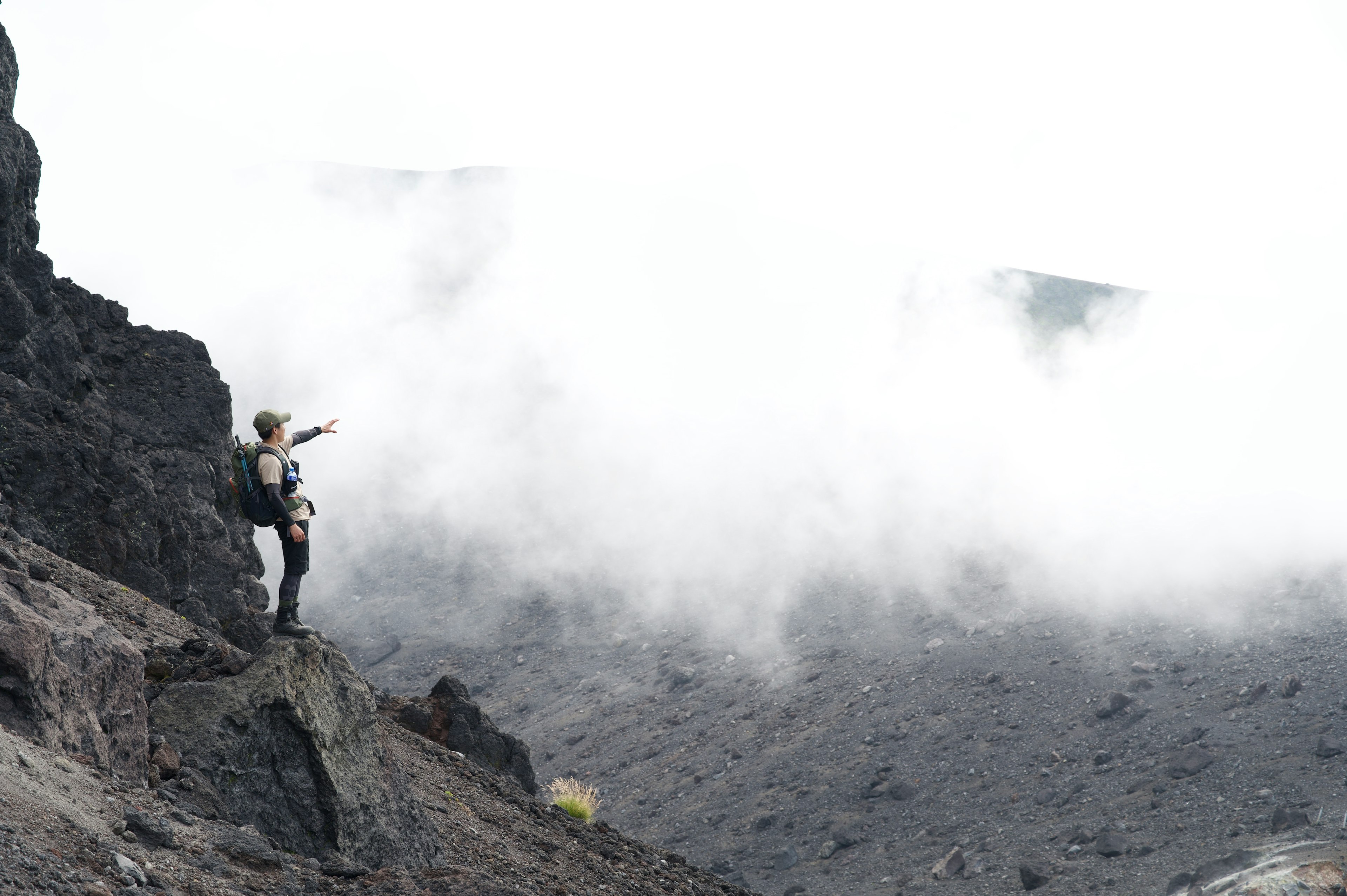 Seseorang berdiri di tepi kawah gunung berapi menunjuk ke arah asap