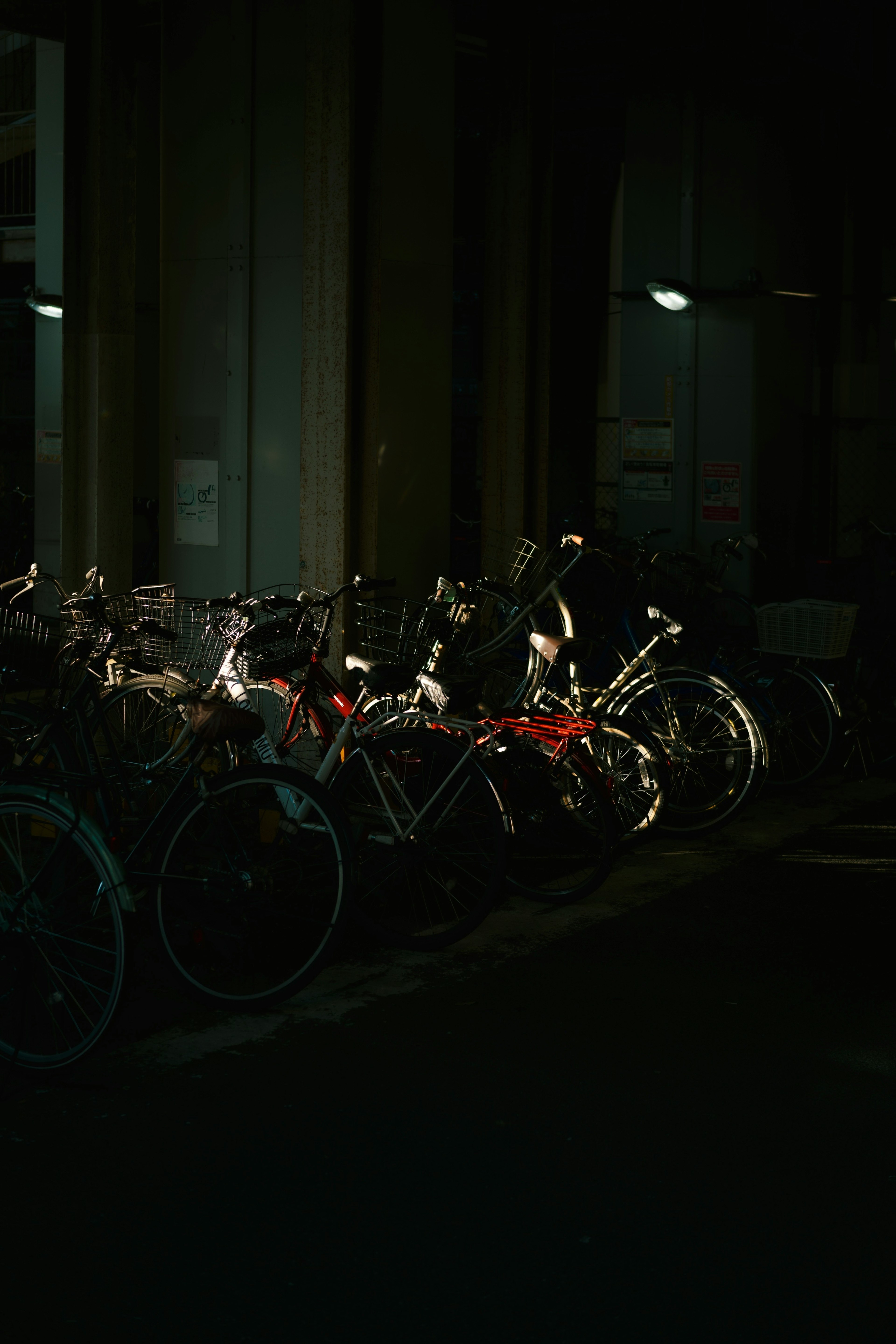 A cluster of bicycles parked in a dimly lit area with surrounding lights