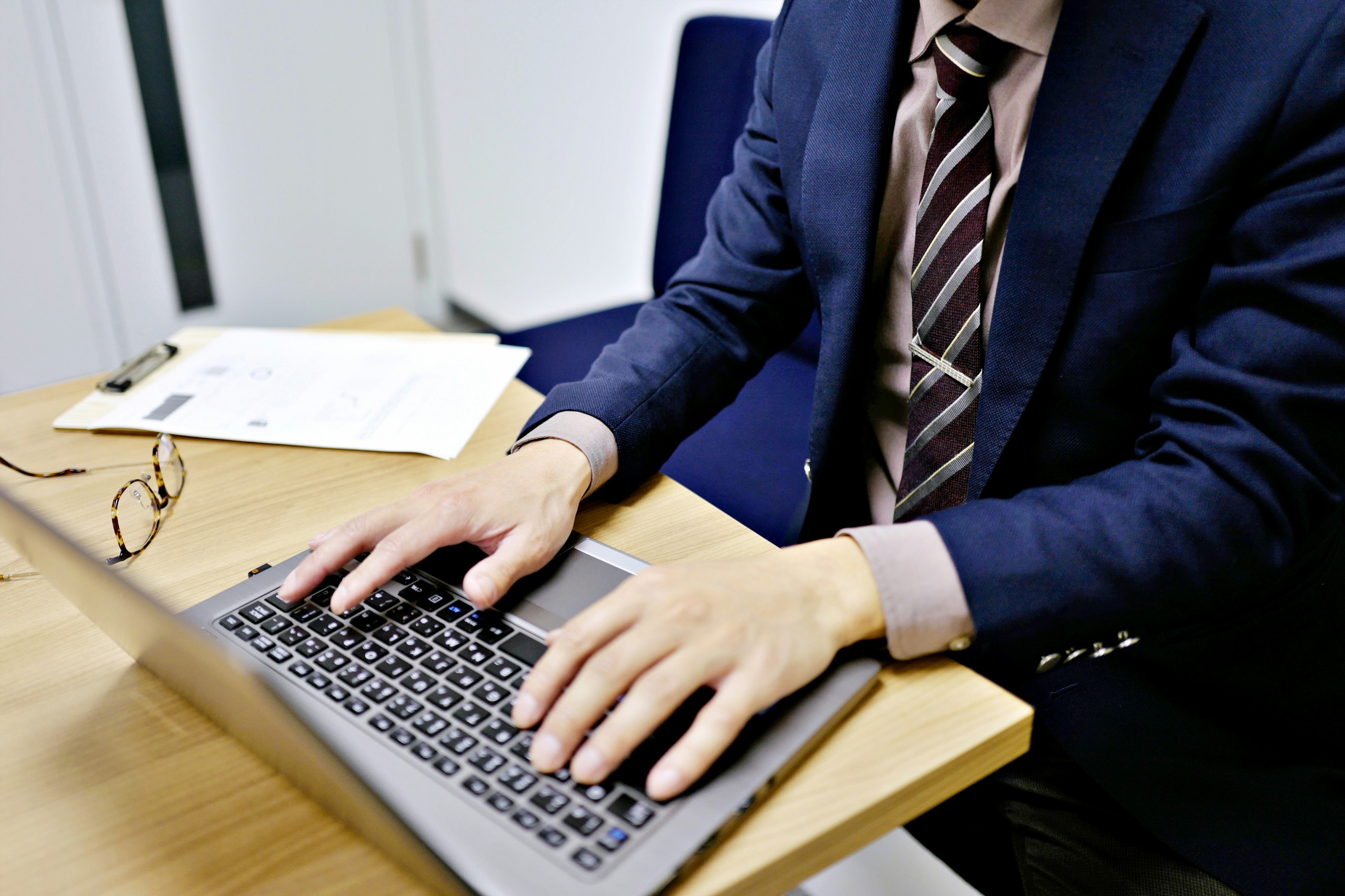 Geschäftsmann arbeitet an einem Laptop mit Unterlagen und Brille auf dem Tisch