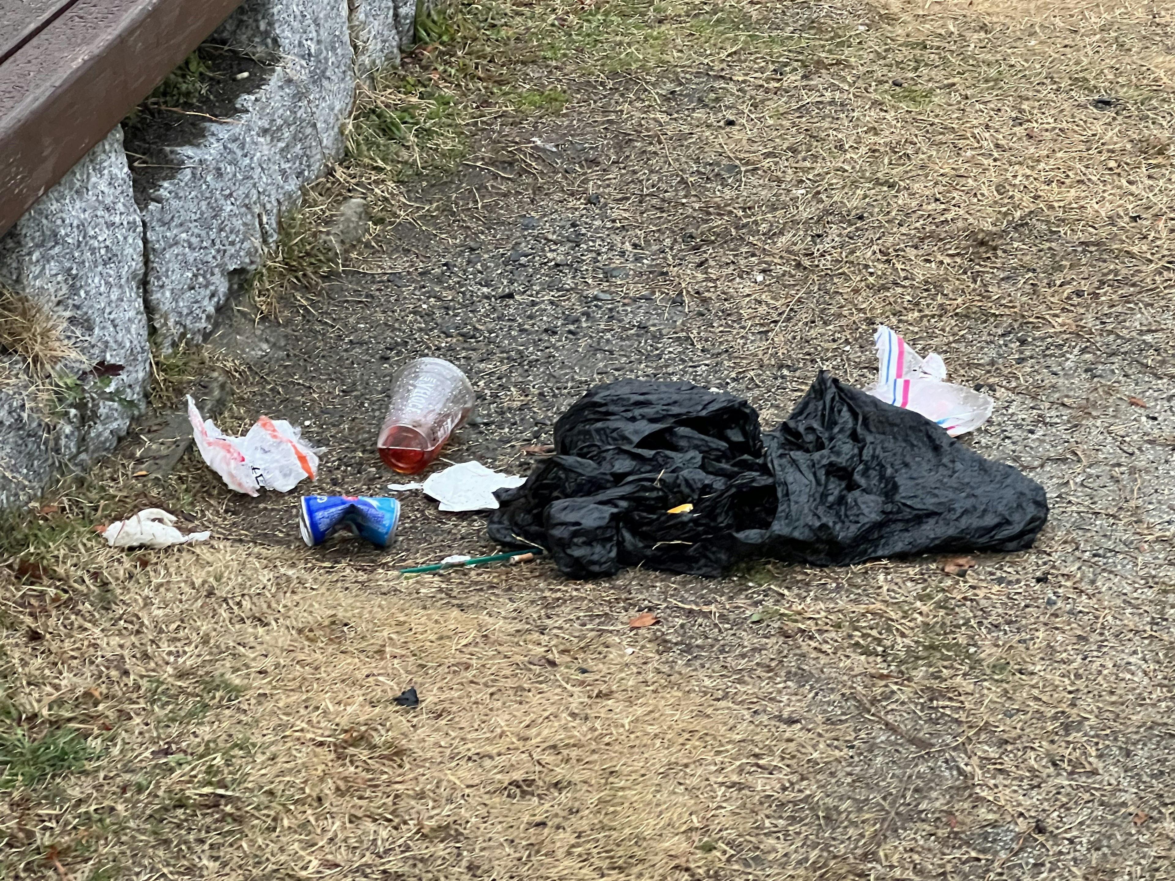 A pile of litter on the ground including a black garbage bag and various trash items