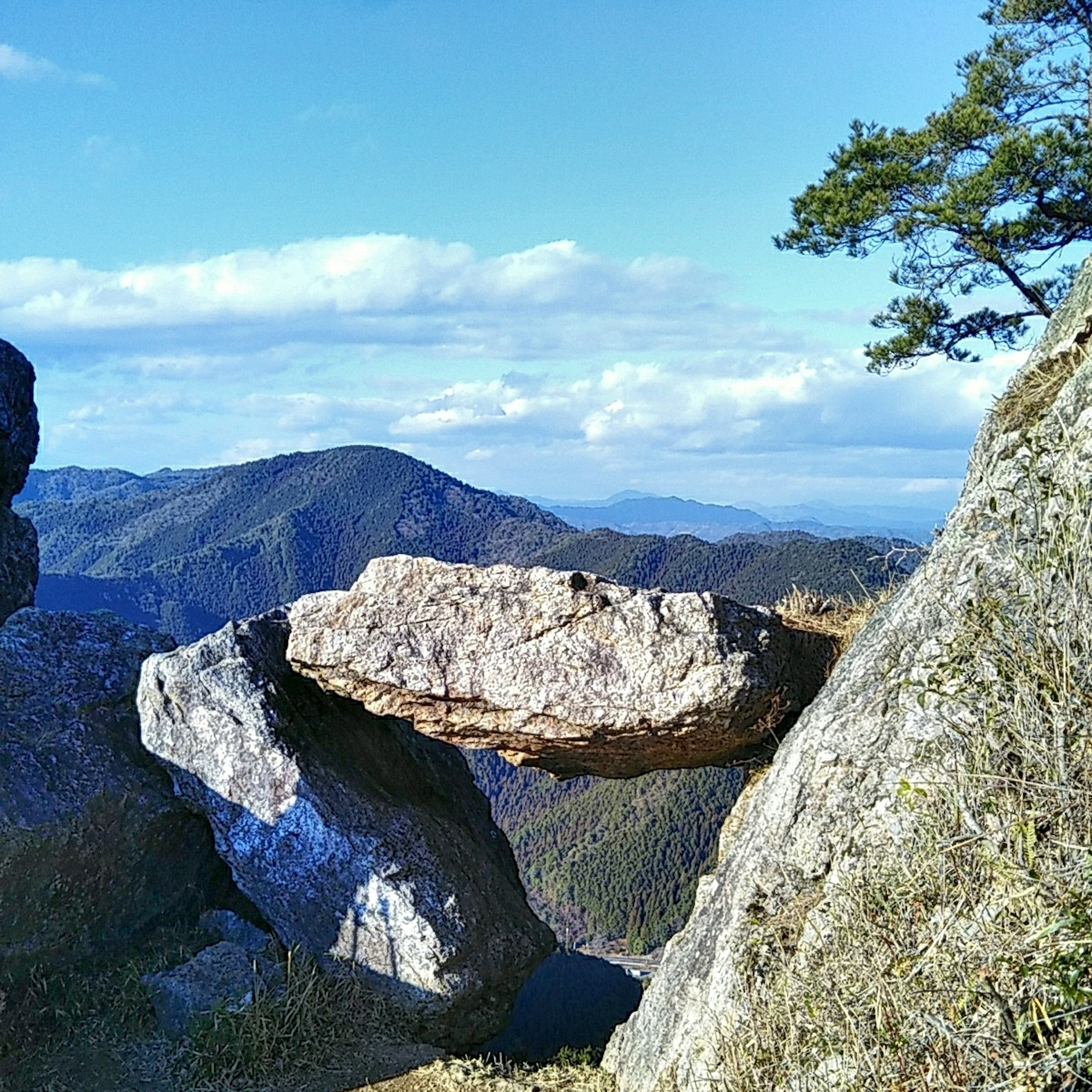 Una gran roca equilibrada sobre una más pequeña con montañas al fondo