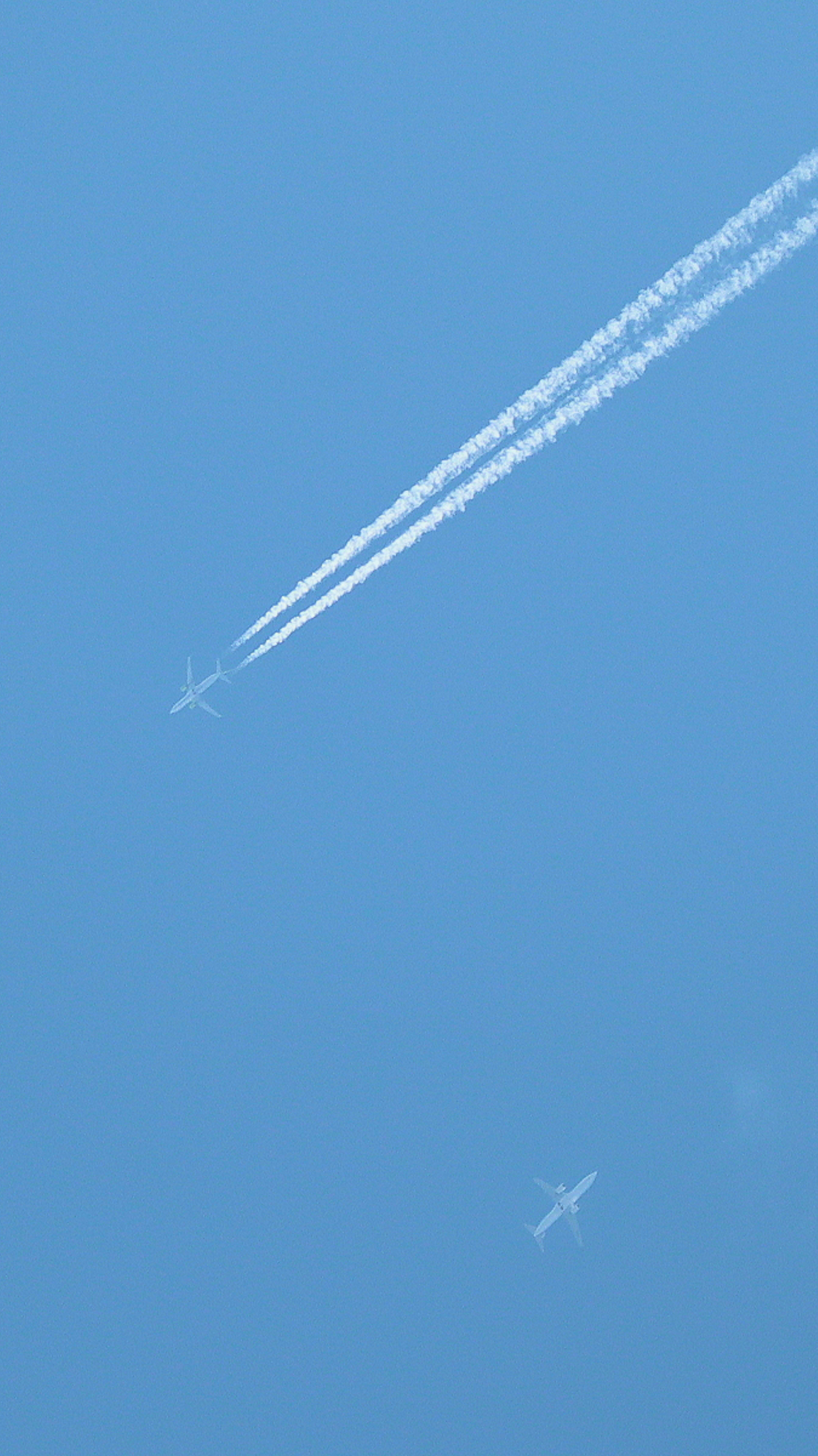 Estelas de un avión en un cielo azul claro con una pequeña aeronave visible