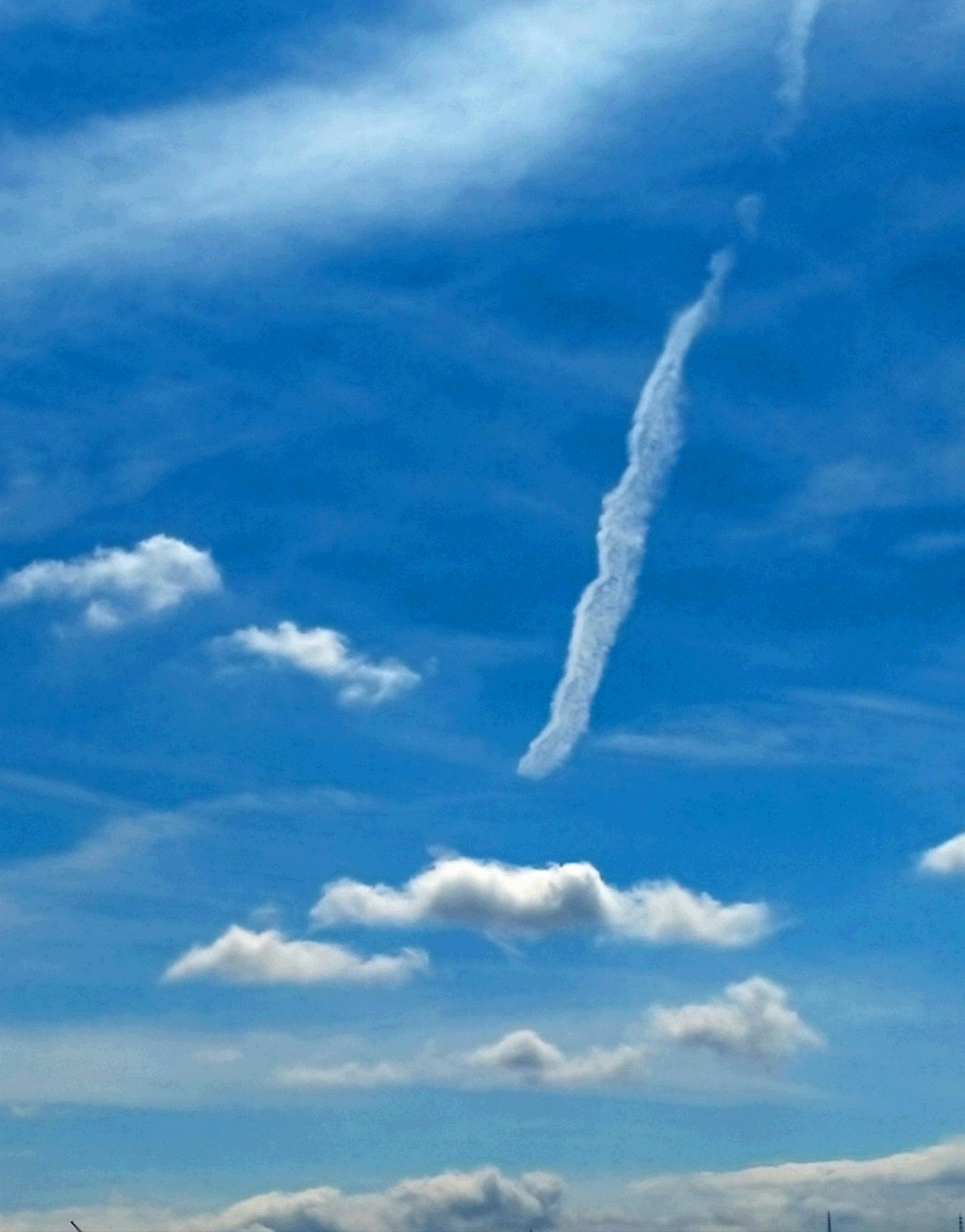 Kontrast von weißen Wolken und einer Kondensstreifen im blauen Himmel