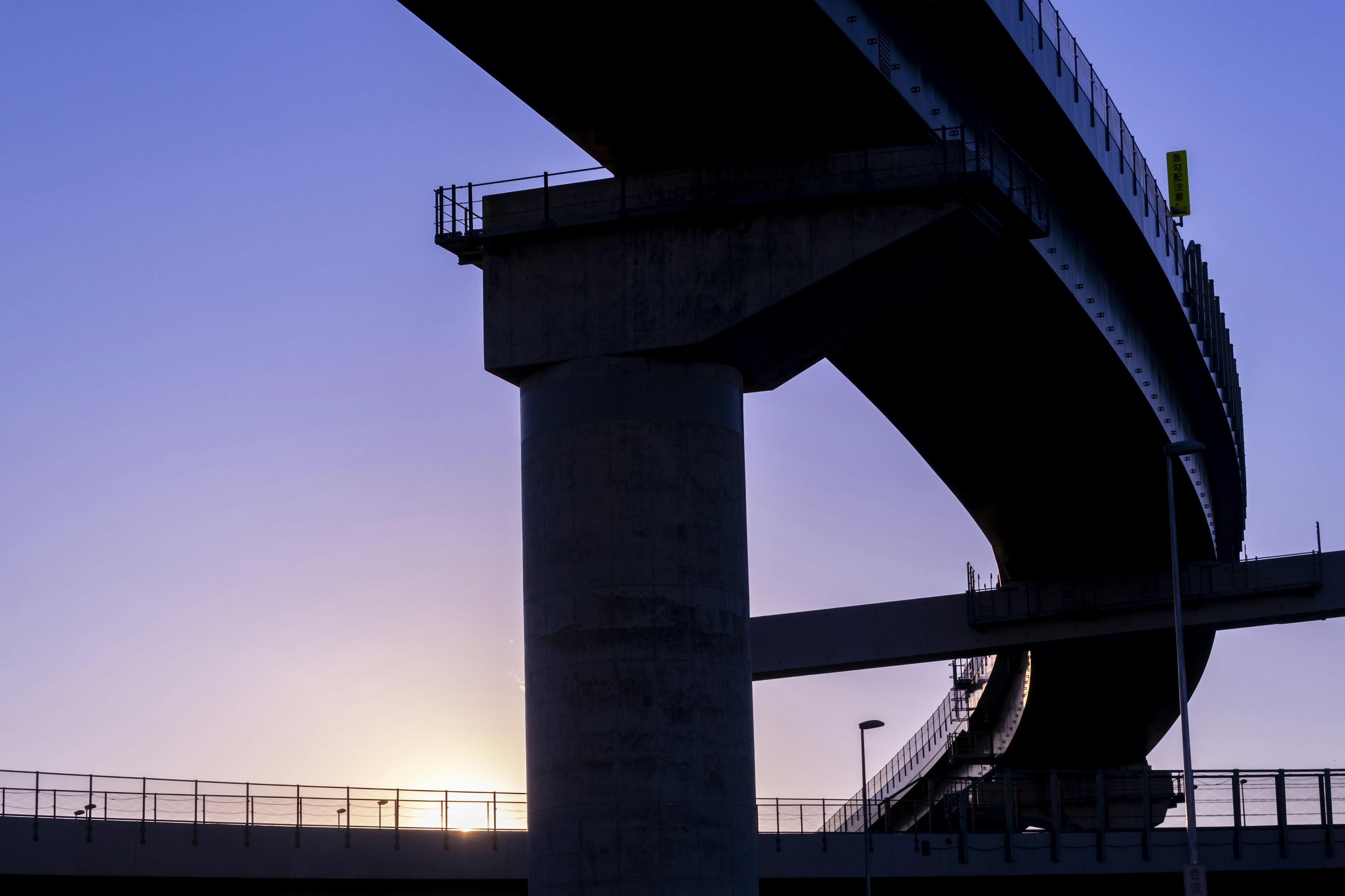 Siluet jembatan dan jalur elevated di latar belakang matahari terbenam yang indah