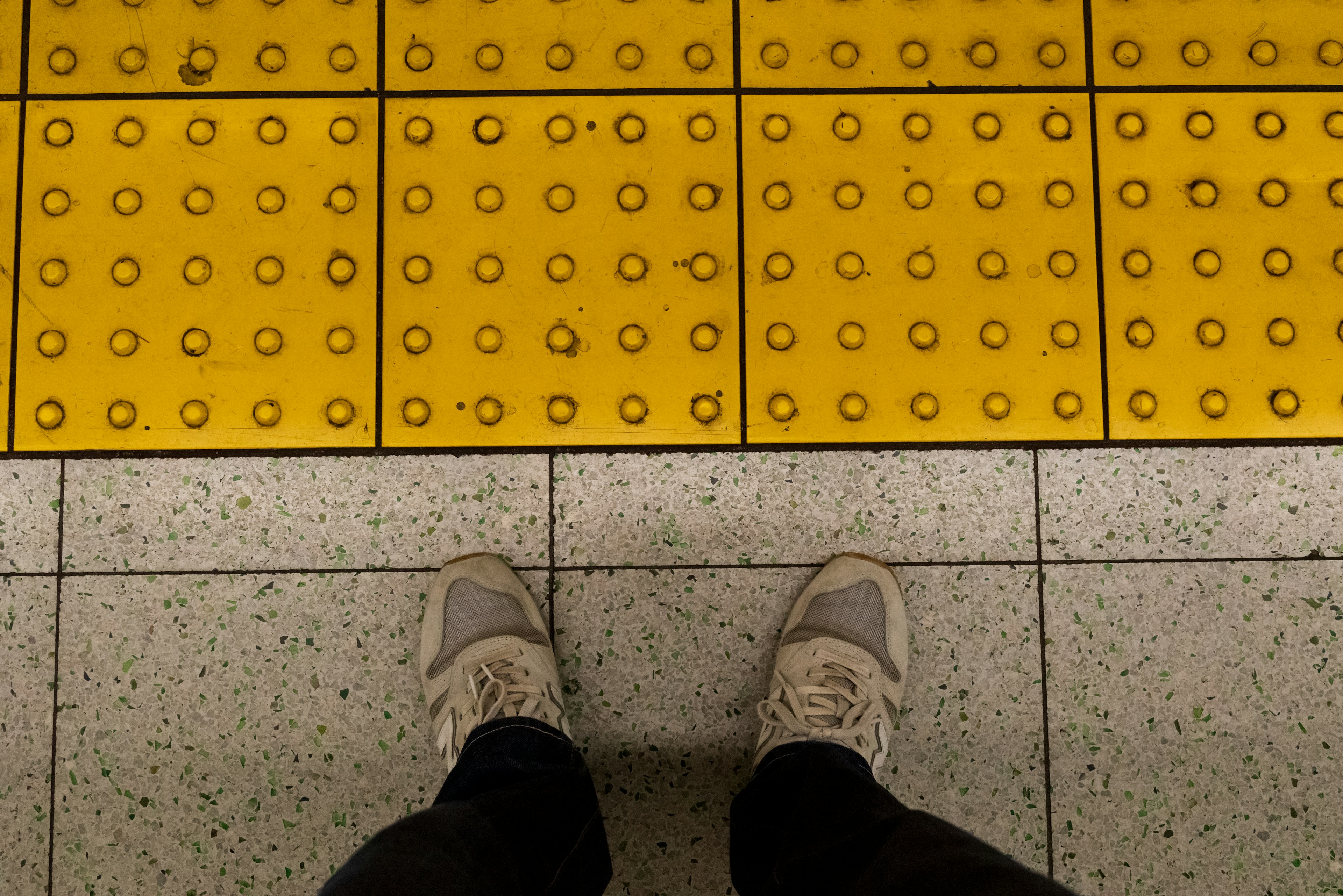 Kaki berdiri di atas paving taktil kuning di stasiun kereta bawah tanah