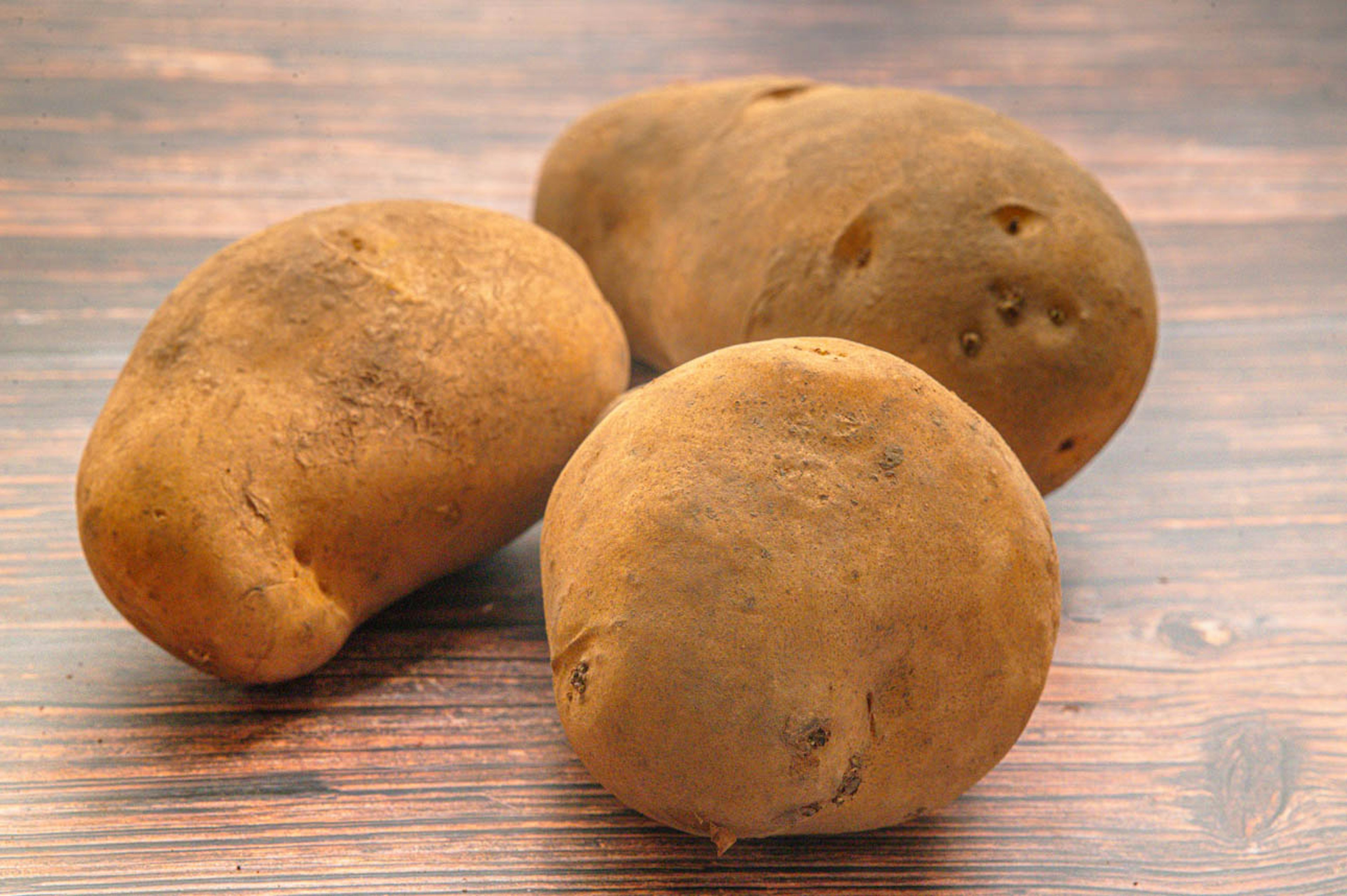 Three potatoes sitting on a wooden table