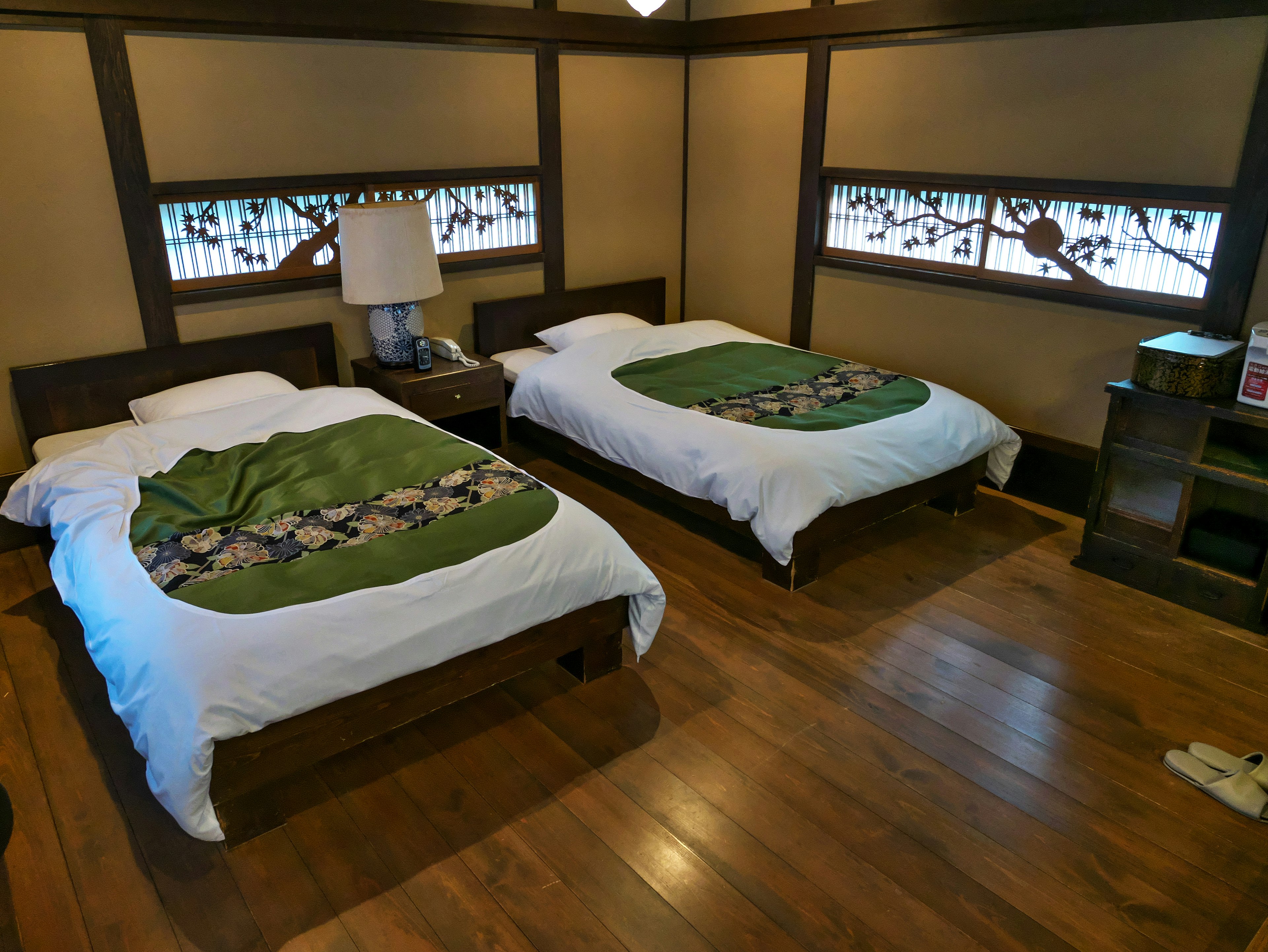 Chambre de style japonais avec deux lits et literie verte sols en bois et vue sur la nature à travers les fenêtres