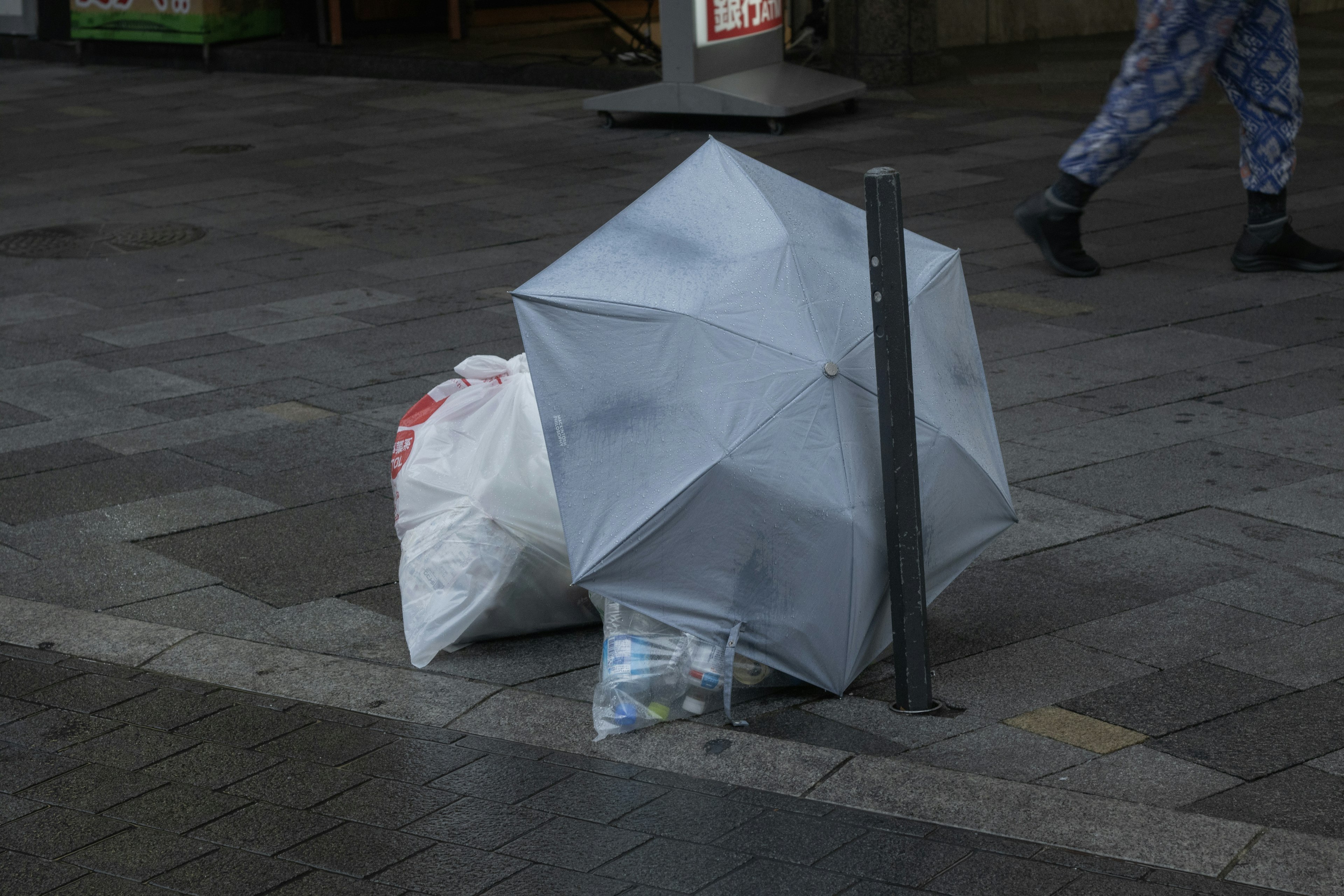 Ein grauer Regenschirm und ein weißer Müllsack auf dem Bürgersteig