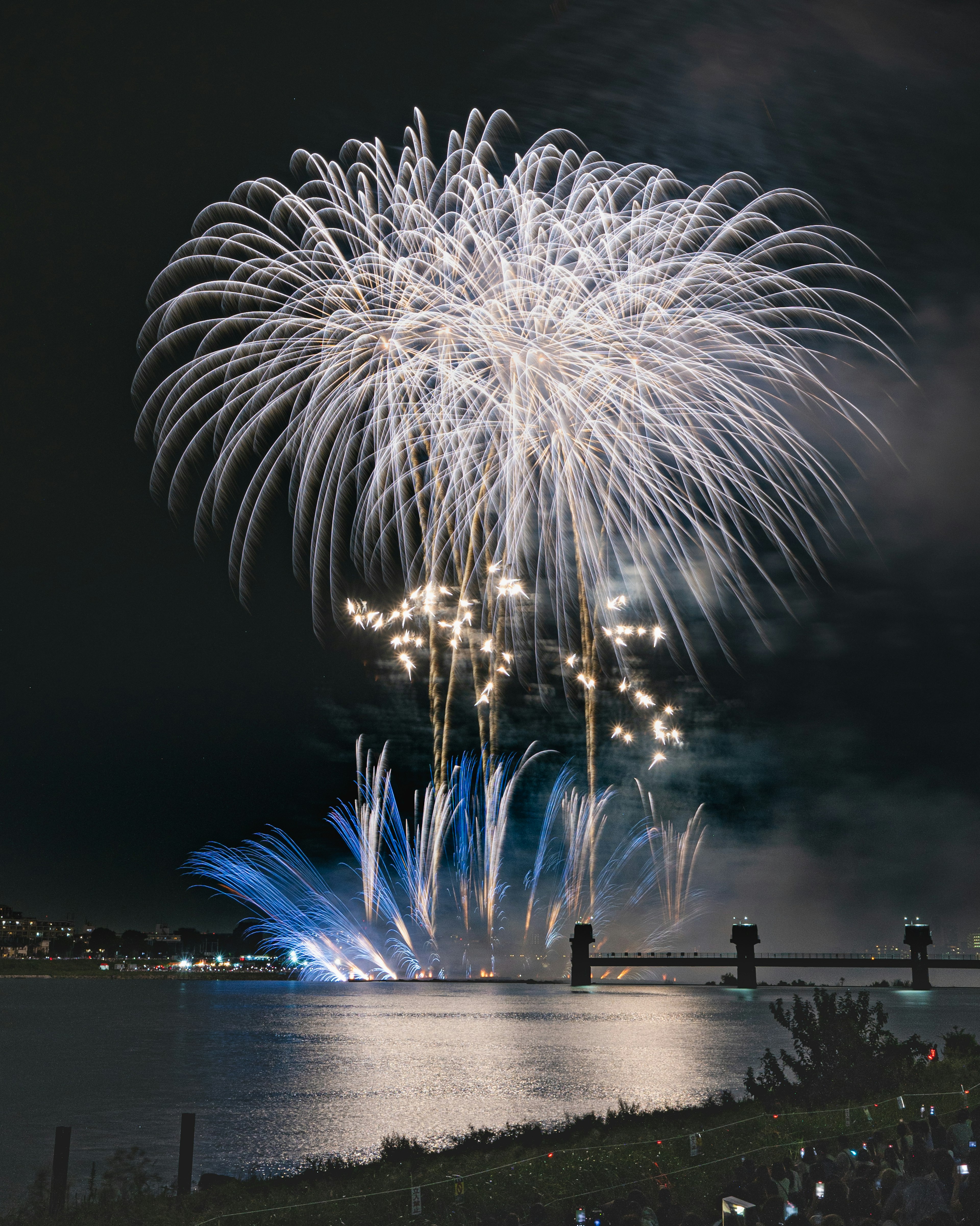 Fireworks in white and blue bursting in the night sky over a river