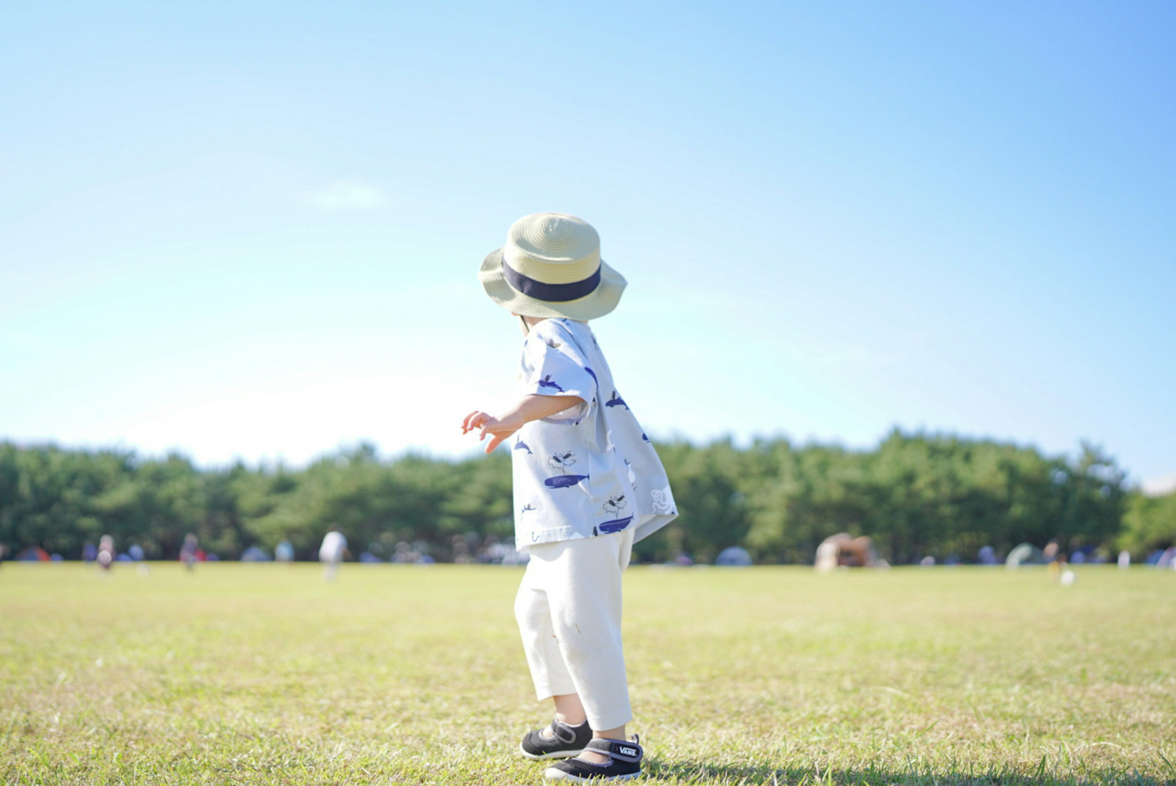 青空の下で草原を走る子供 白いパンツと帽子を着用