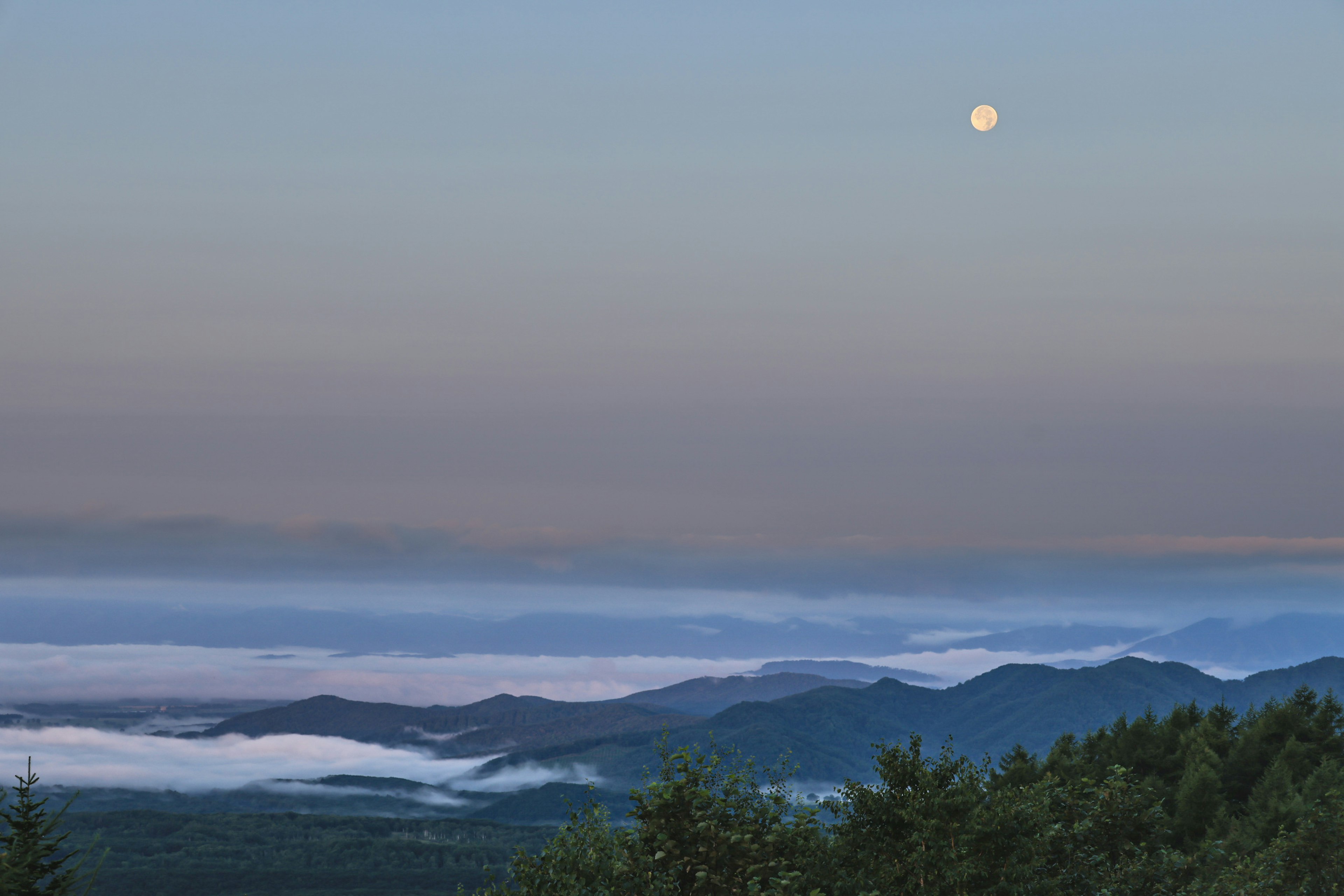 Luna che sorge su montagne nebbiose con un cielo sereno serale