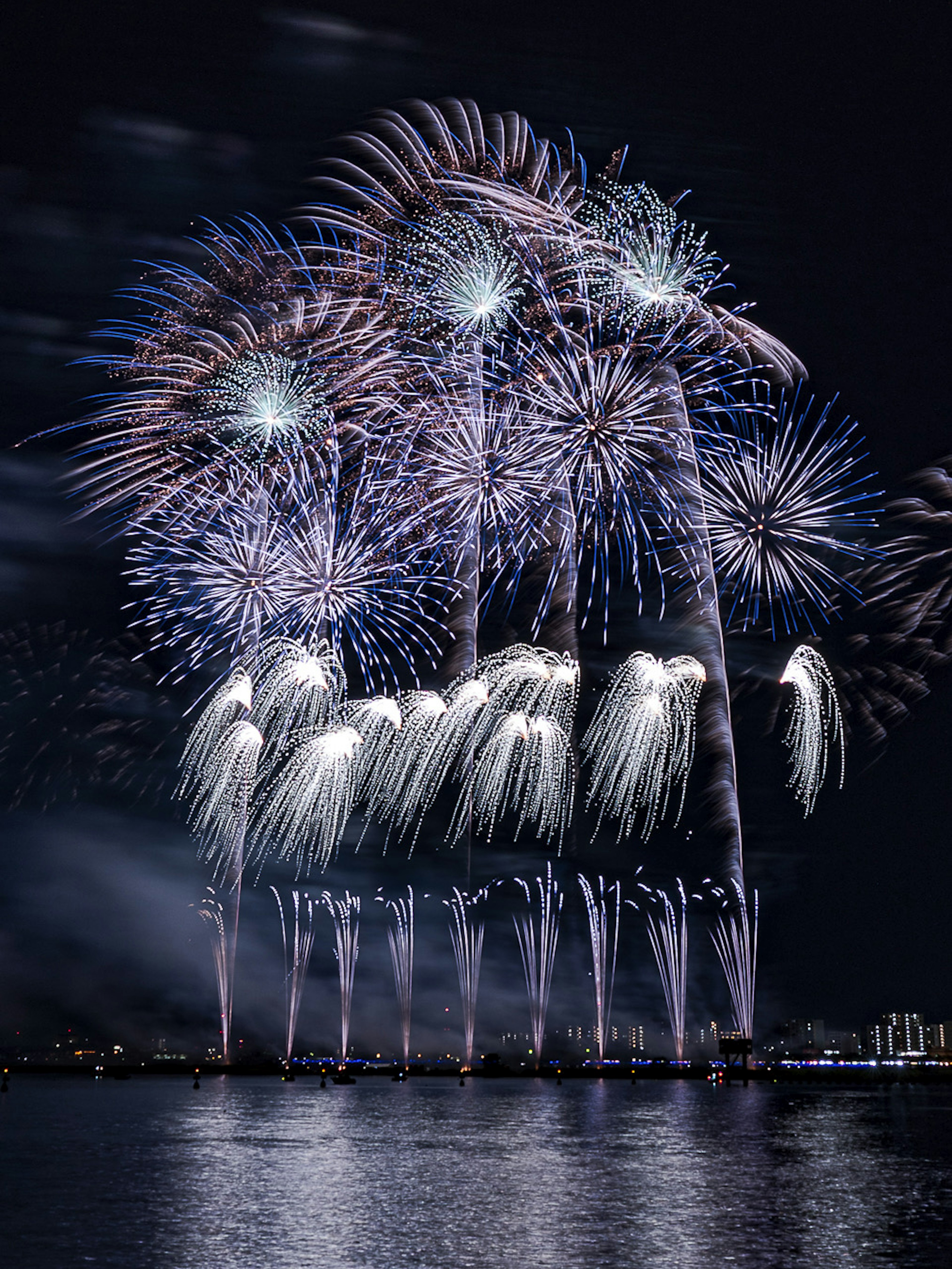 Spettacolo di fuochi d'artificio colorati che illumina il cielo notturno con riflessi sull'acqua