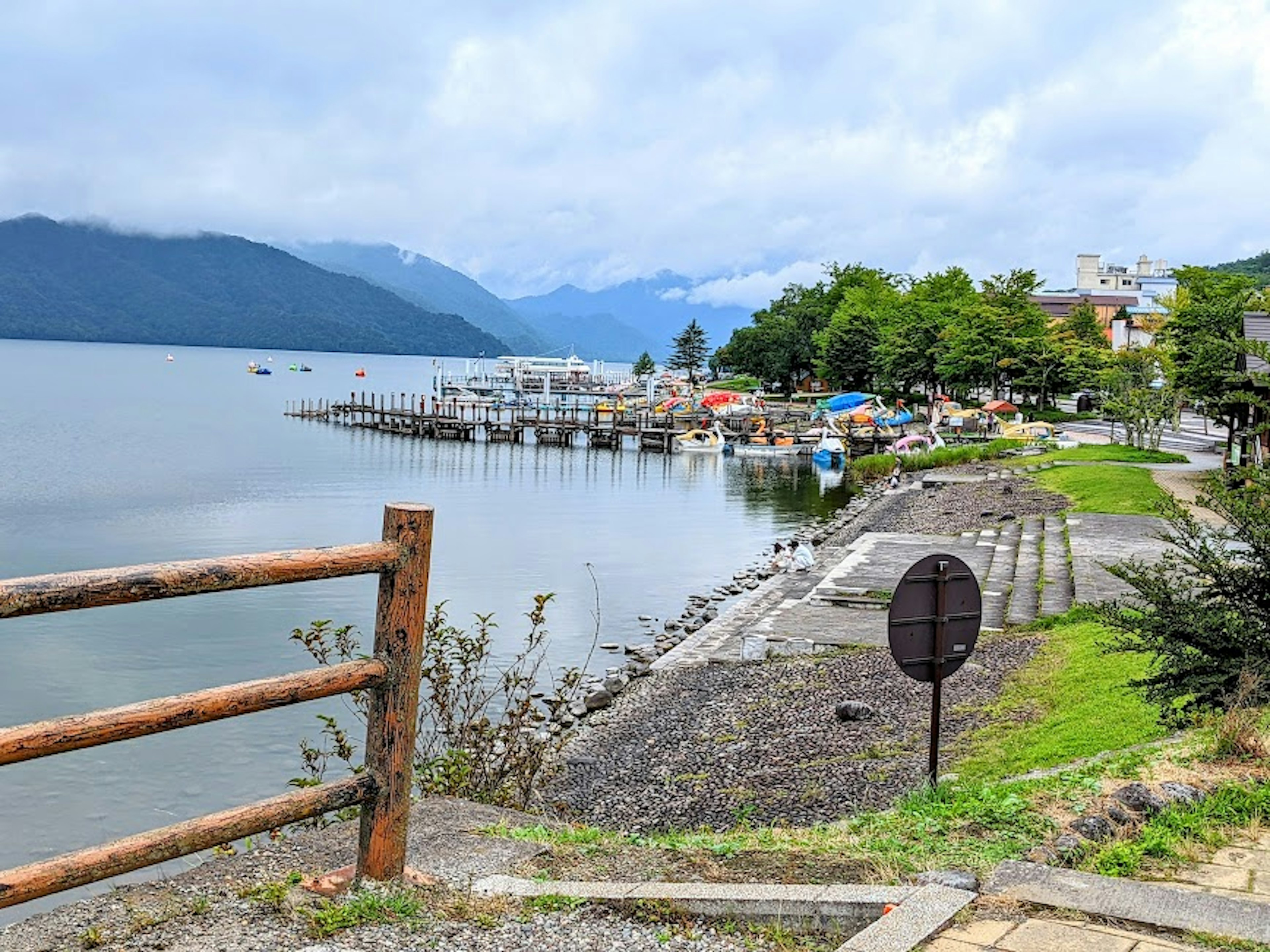 Danau tenang dengan gunung di latar belakang, menampilkan dermaga dan jalur