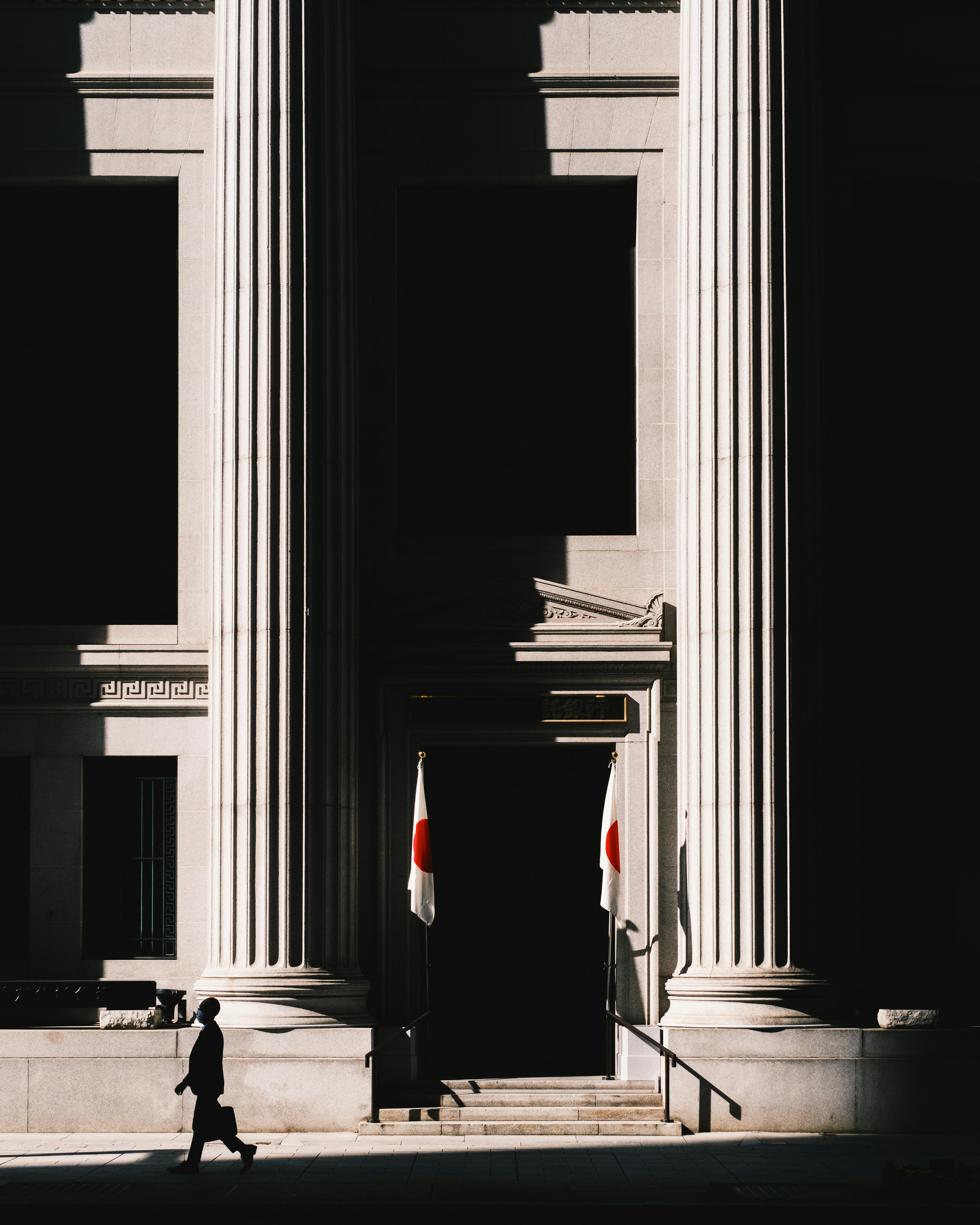 Person walking in front of a building with large columns and a dark entrance