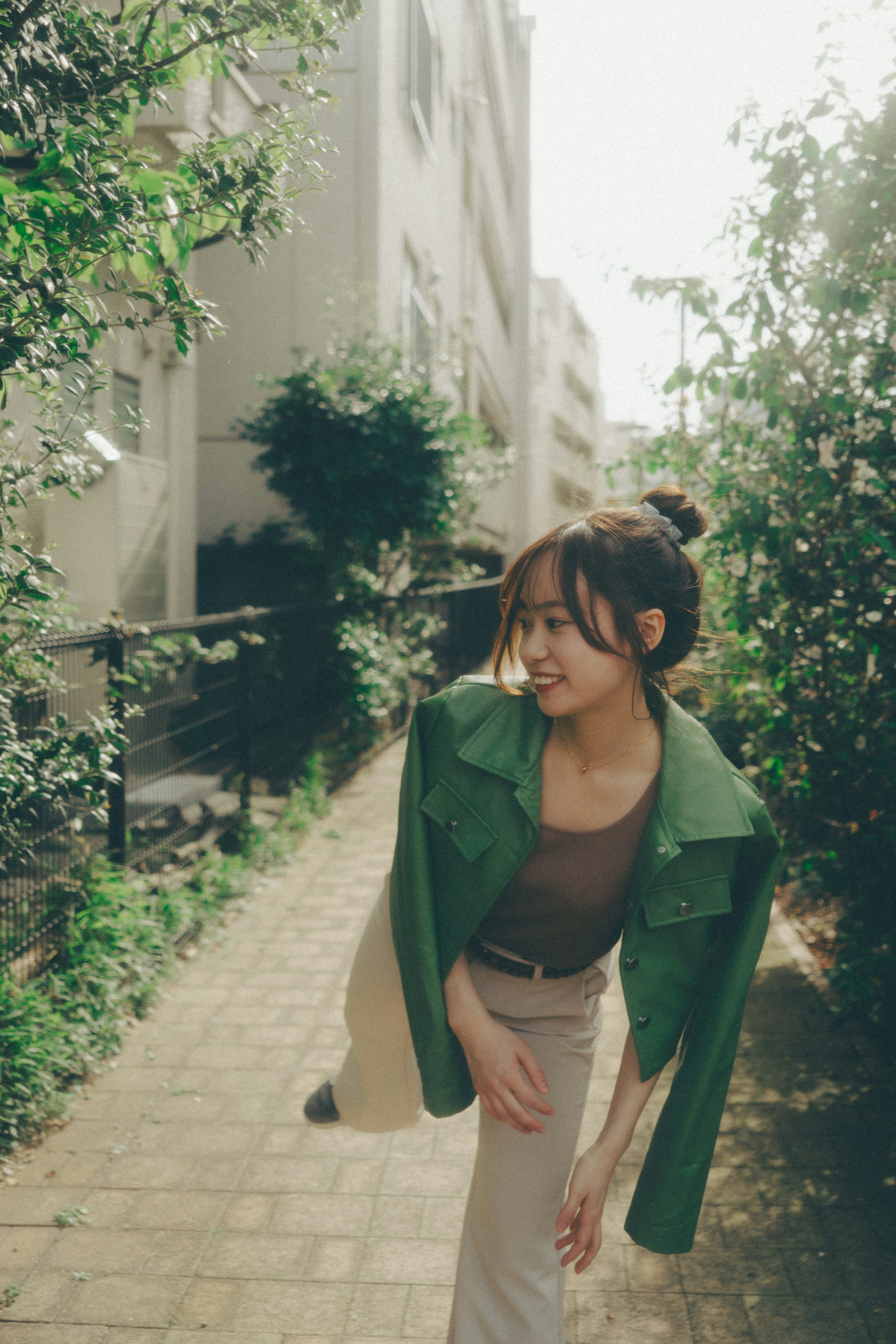 A woman in a green jacket walking along a path surrounded by greenery