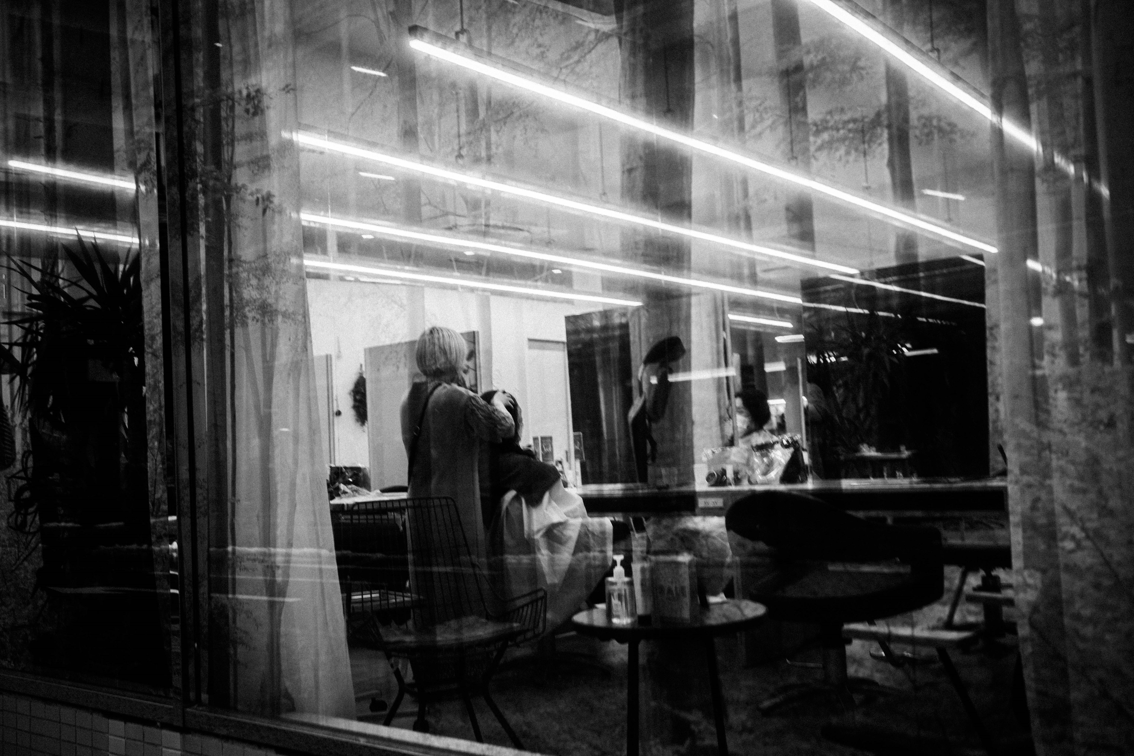 Interior of a hair salon seen through a window with a woman getting a haircut and stylist