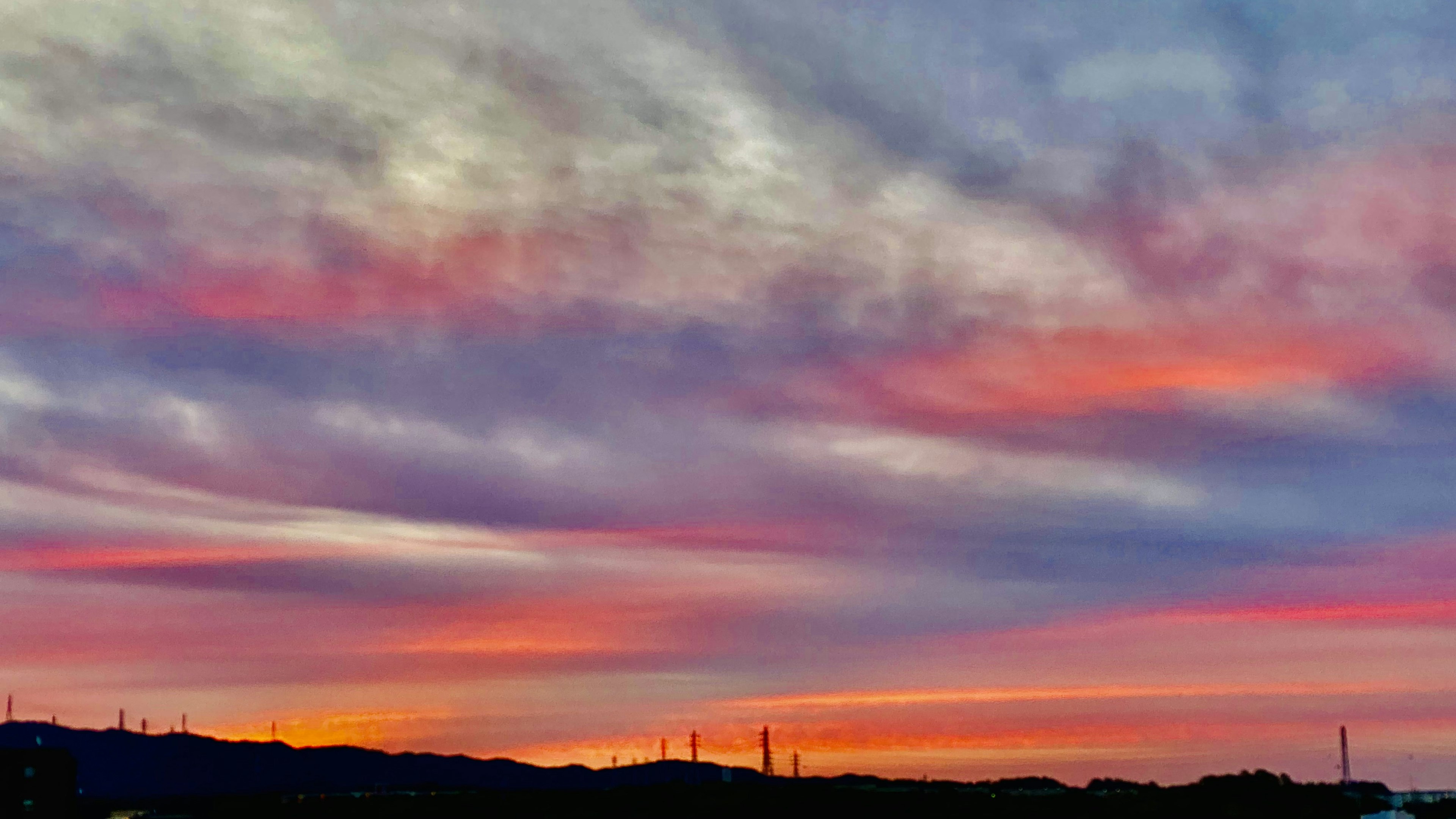 Cielo de atardecer vibrante con nubes coloridas y siluetas de colinas