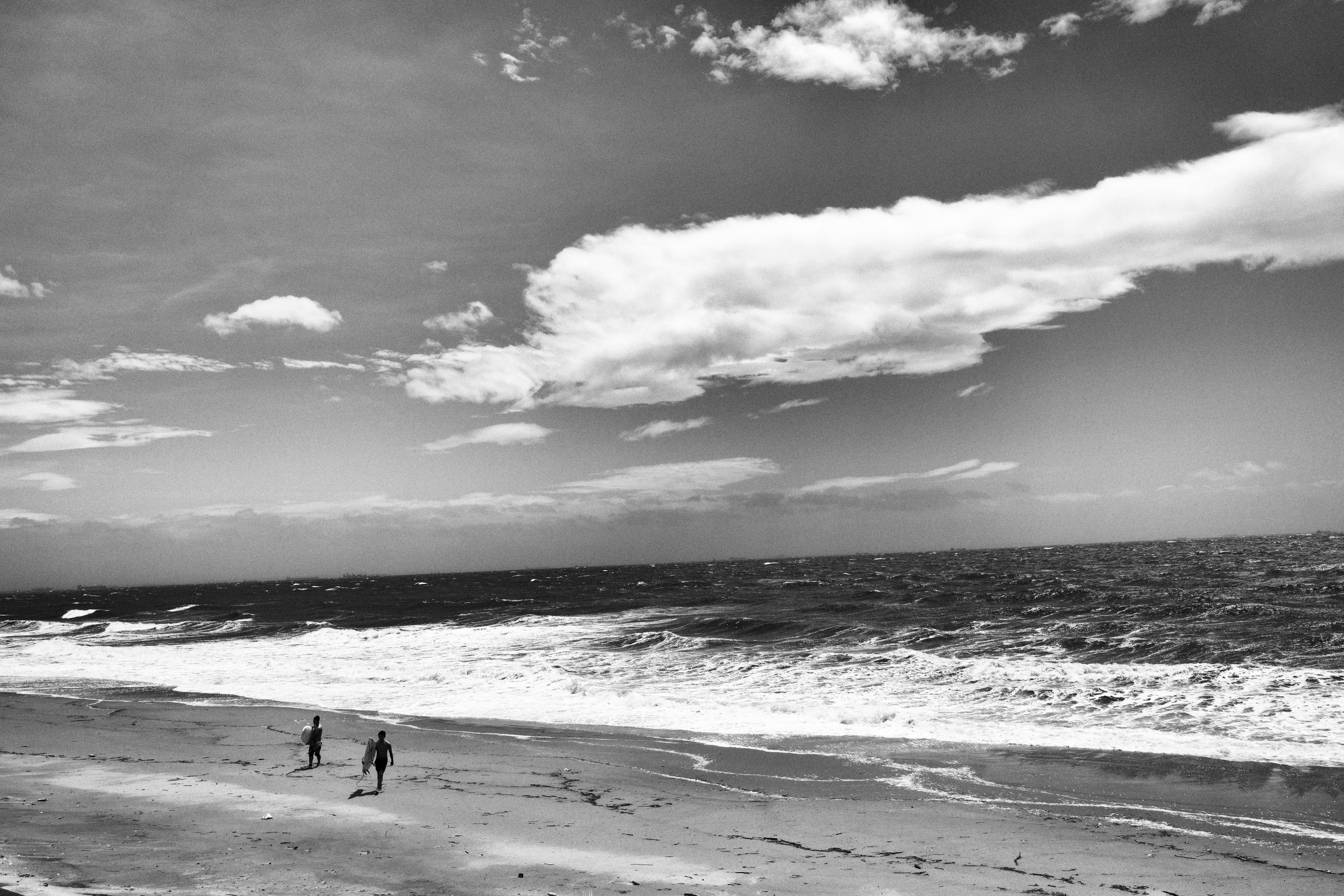 Siluetas de dos personas caminando en una playa en blanco y negro con olas