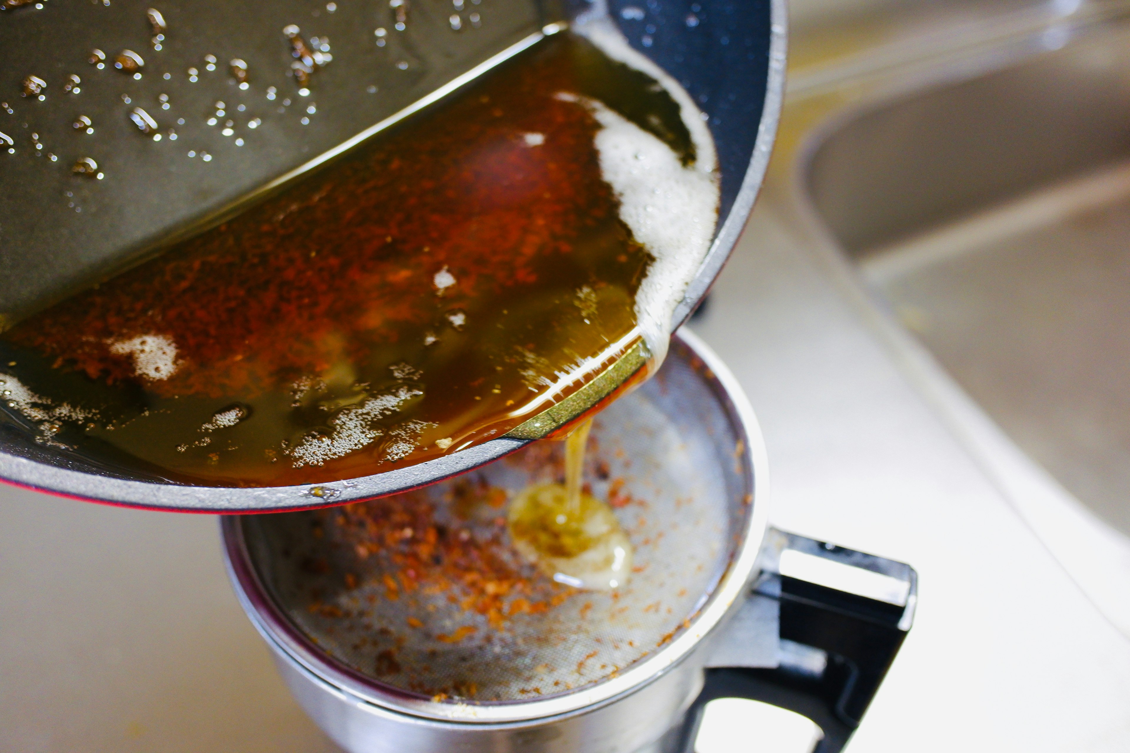 Pouring oil through a strainer into a container